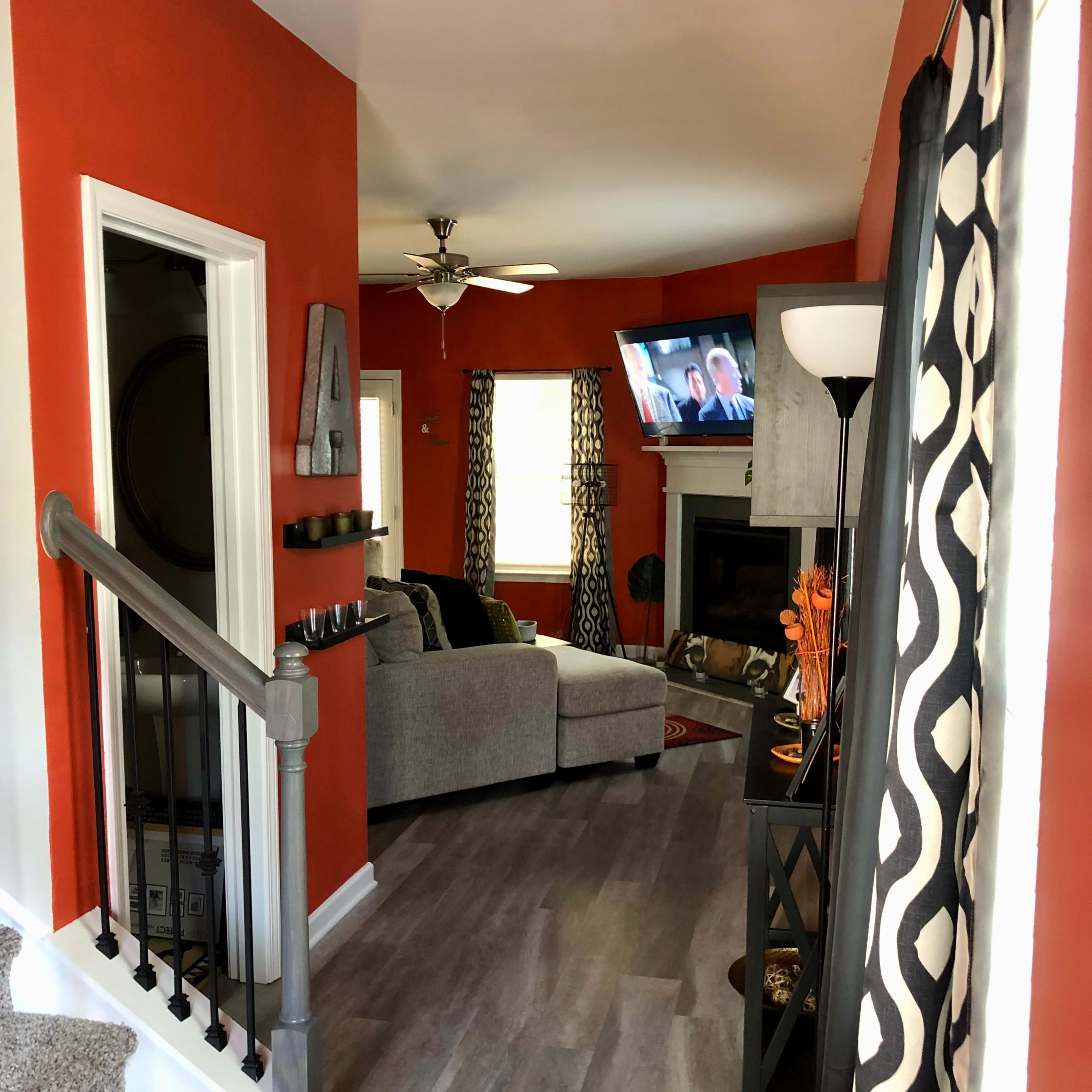 A living area with an orange wall, a gray couch facing a television, and a staircase leading to another level.