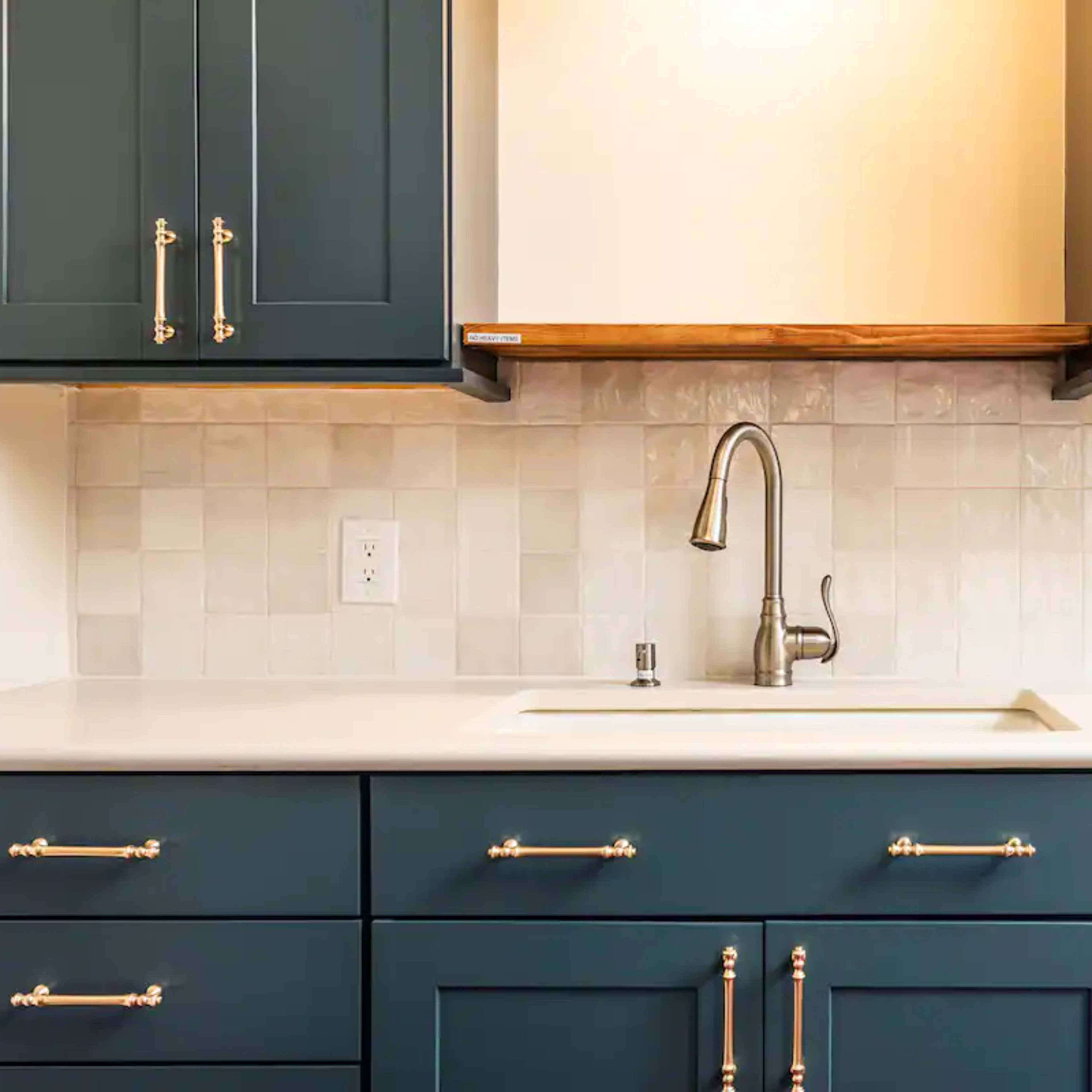 A kitchen sink area with dark blue cabinets, a white countertop, and a tile backsplash.