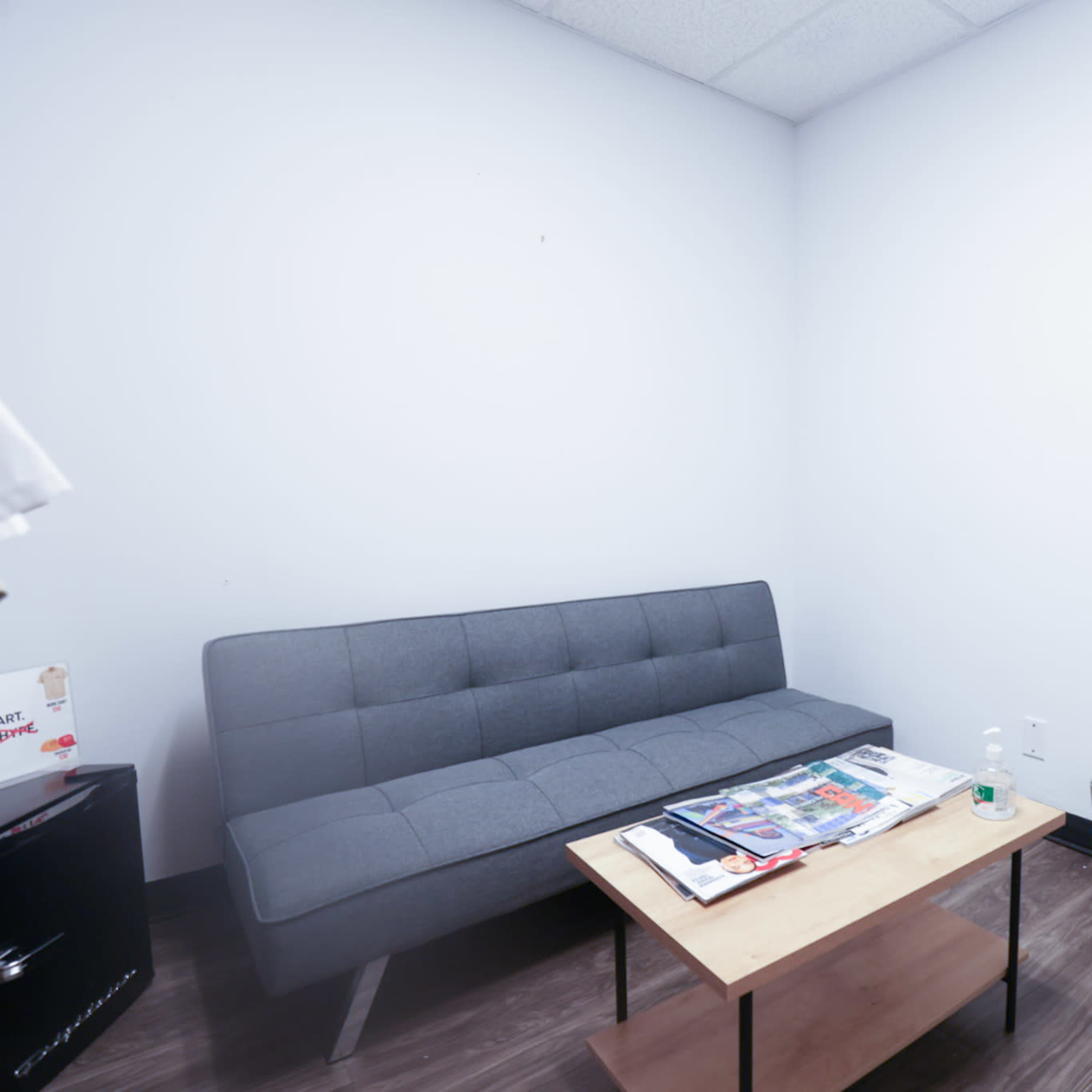 A small waiting room with a gray sofa, a wooden coffee table with magazines, and a door leading outside.