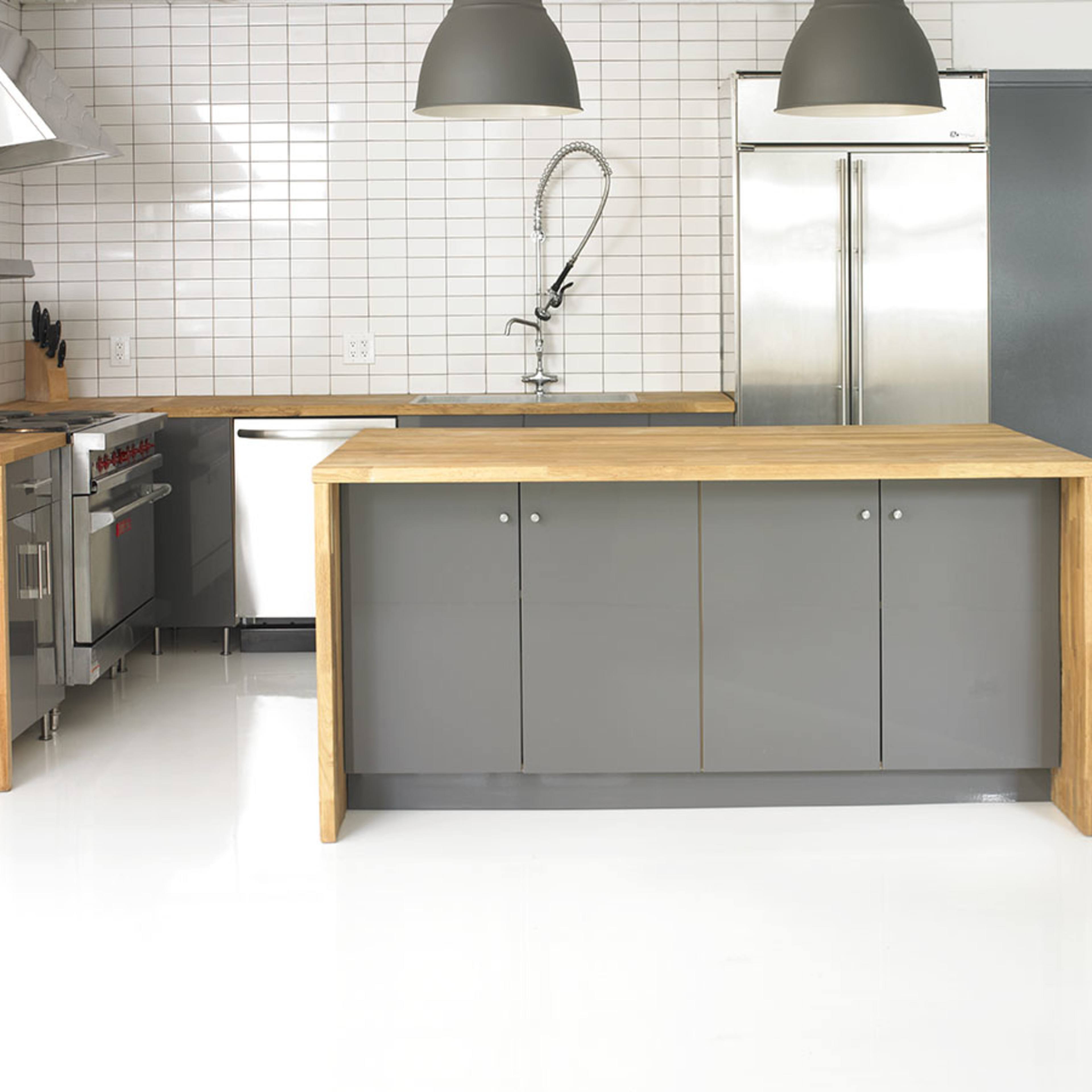 A modern kitchen features a stainless steel range, a wood-topped island, and gray cabinetry against a tiled wall.