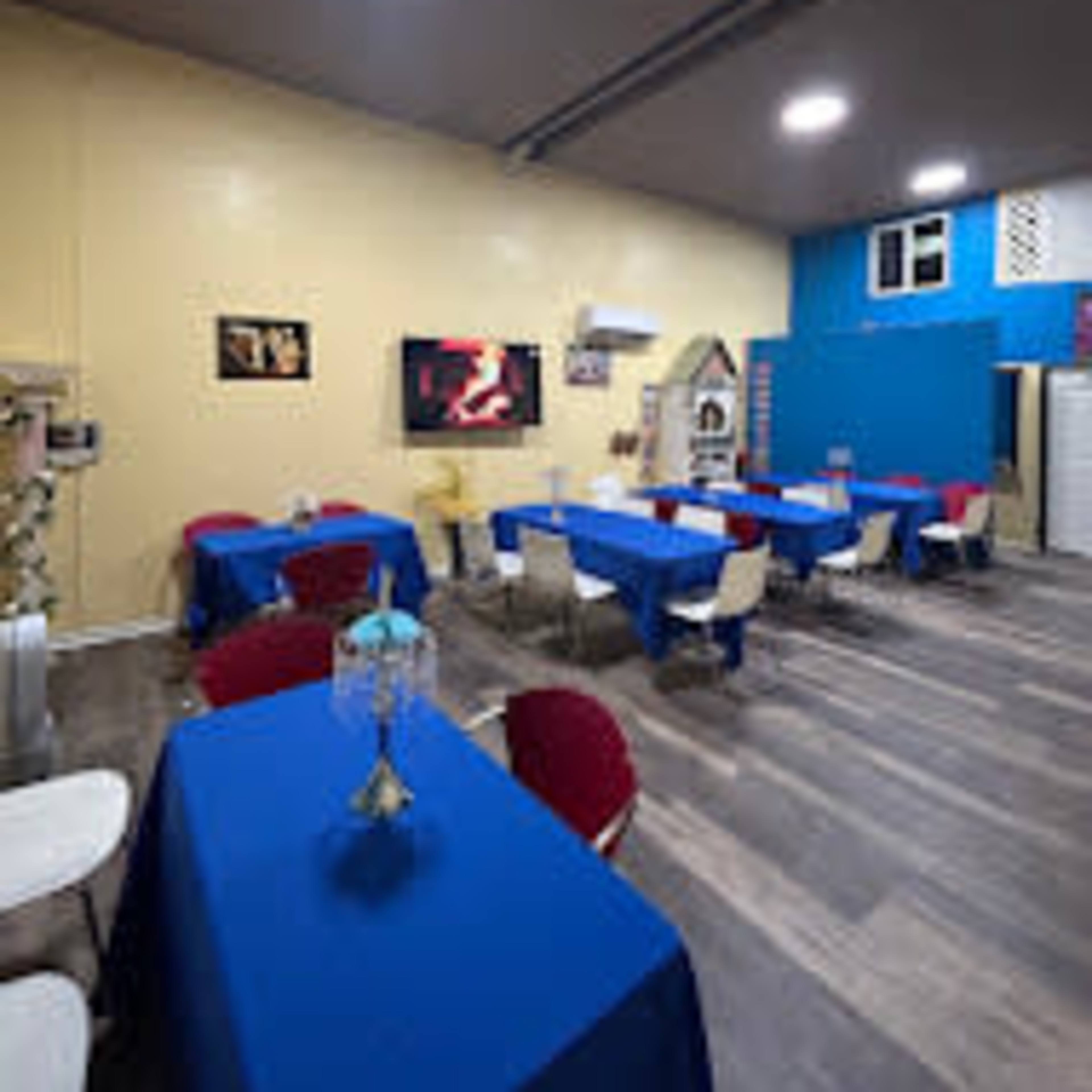 A dining area with blue and red tablecloths covering several tables, a television on the wall, and a mix of chair styles.