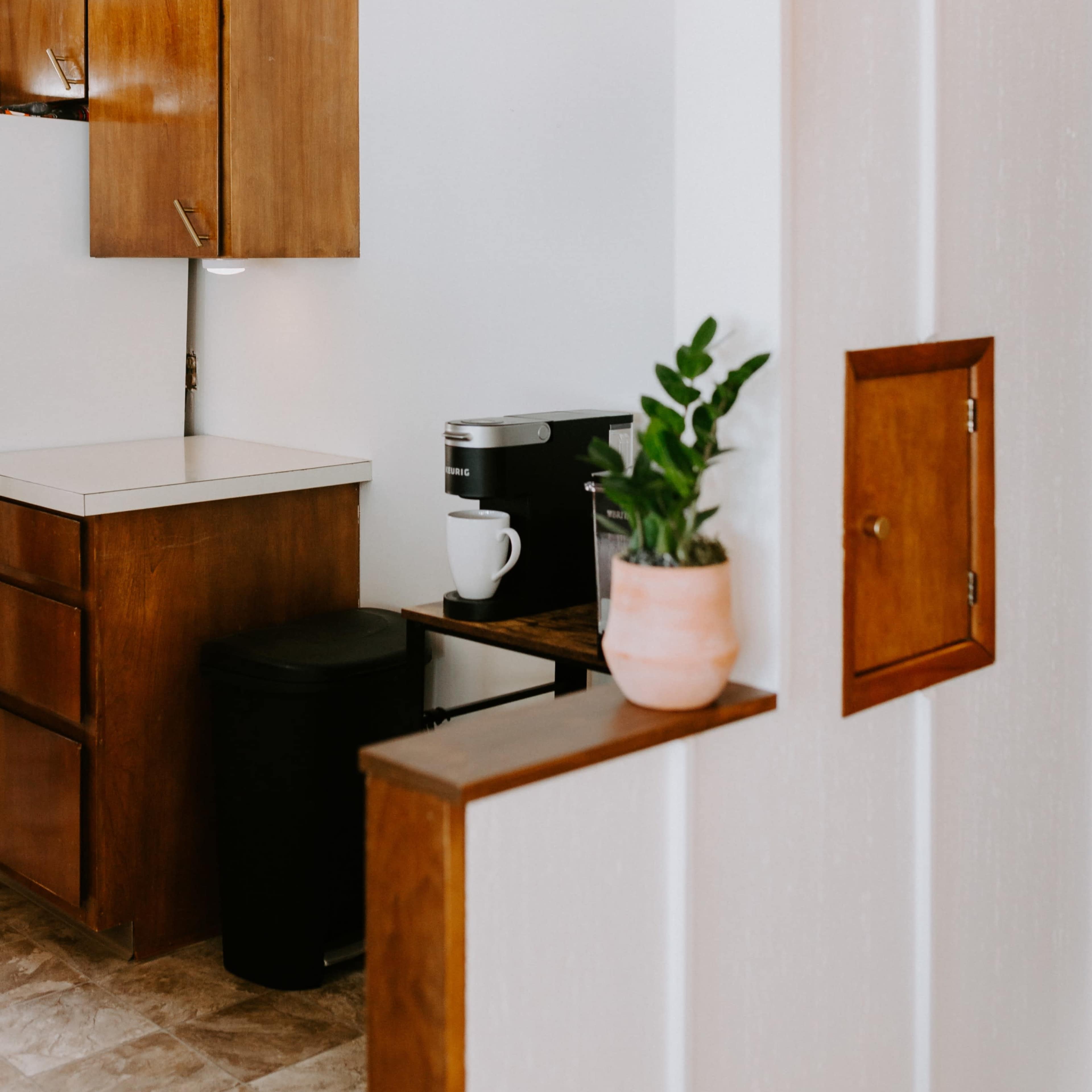 A modern kitchen with wooden cabinets, a coffee maker, a white countertop, and a small plant on a counter.