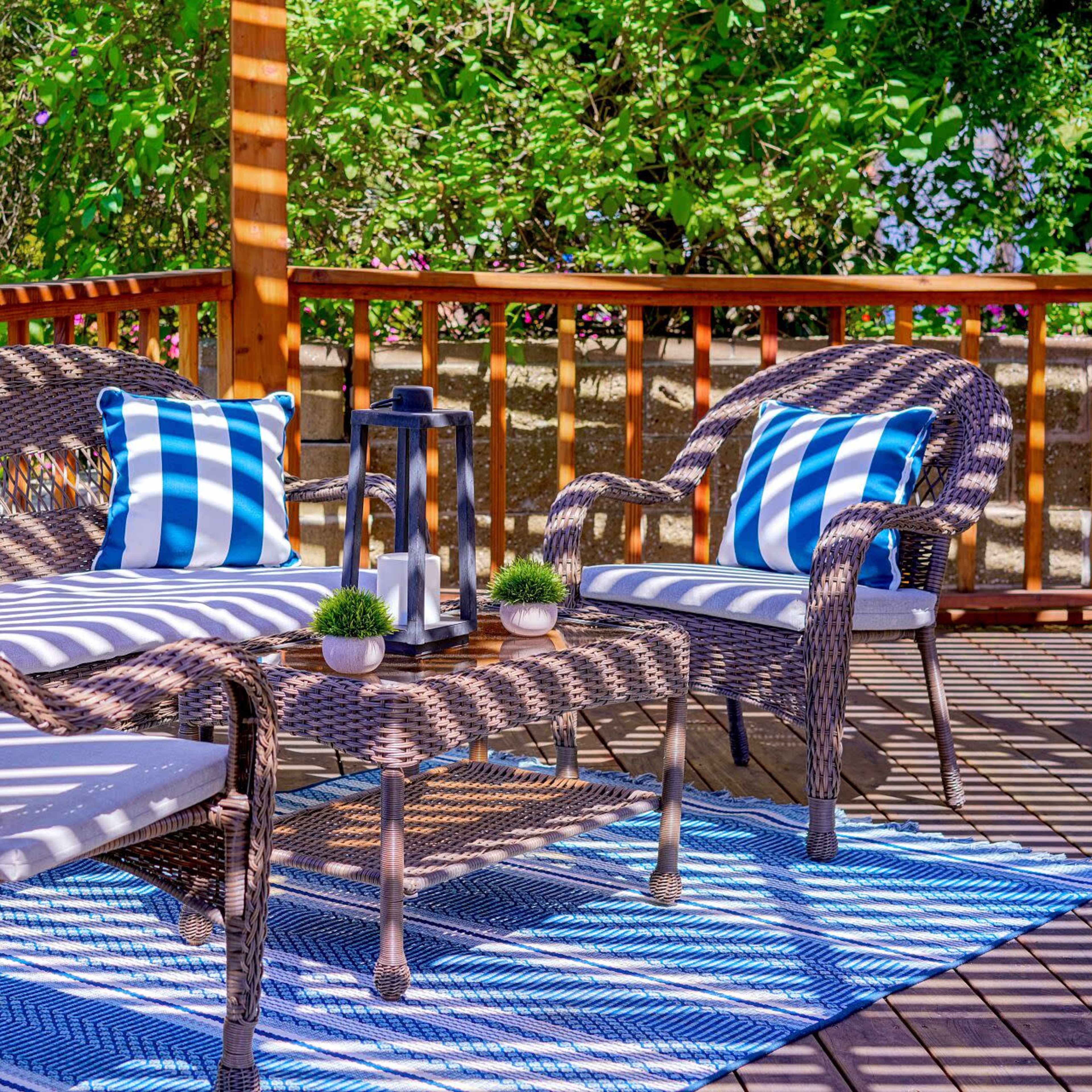 A seating area on a deck features woven furniture with blue and white striped cushions, a coffee table, and small decorative plants.