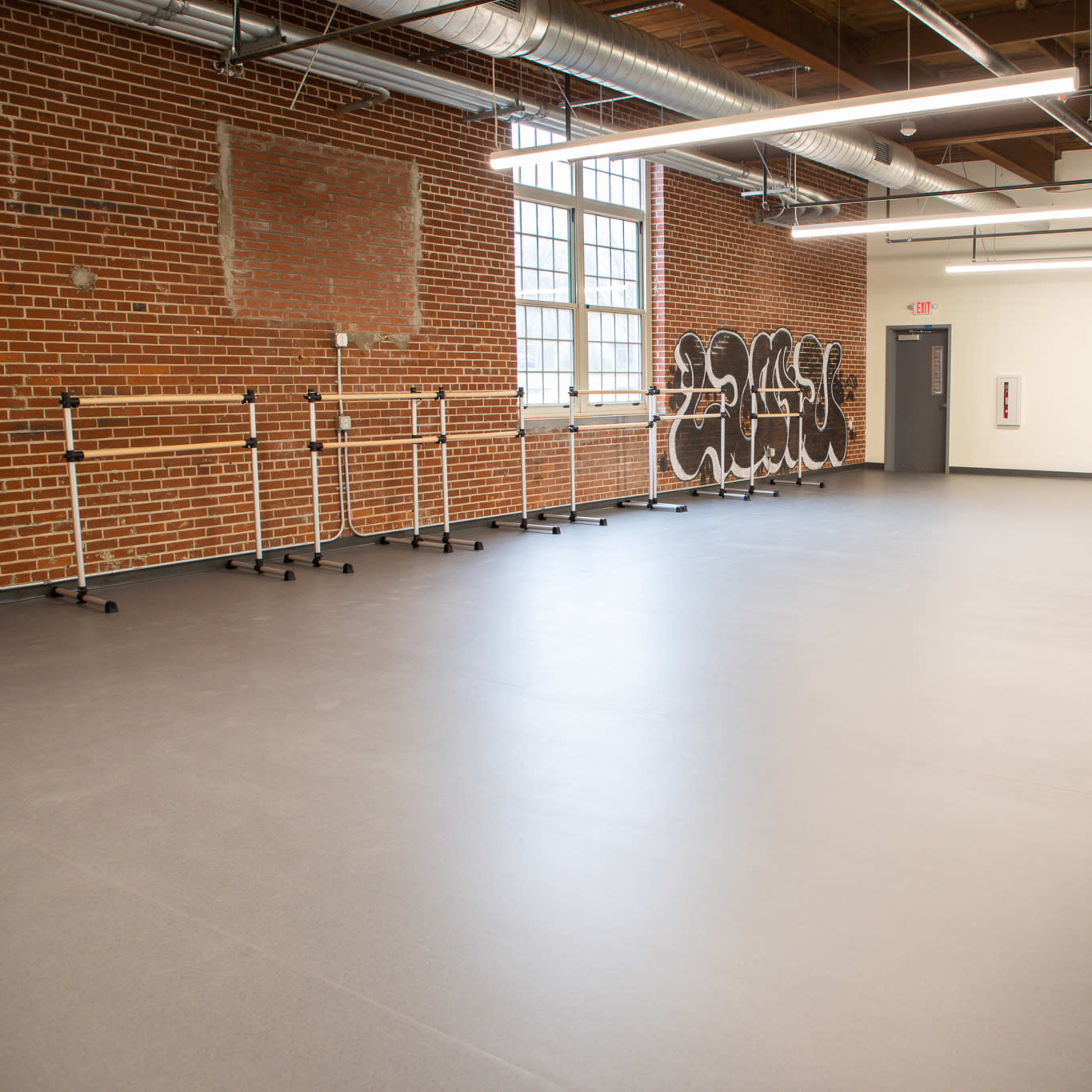 A spacious dance studio with wooden beams, exposed brick walls, and several ballet barres along one side.