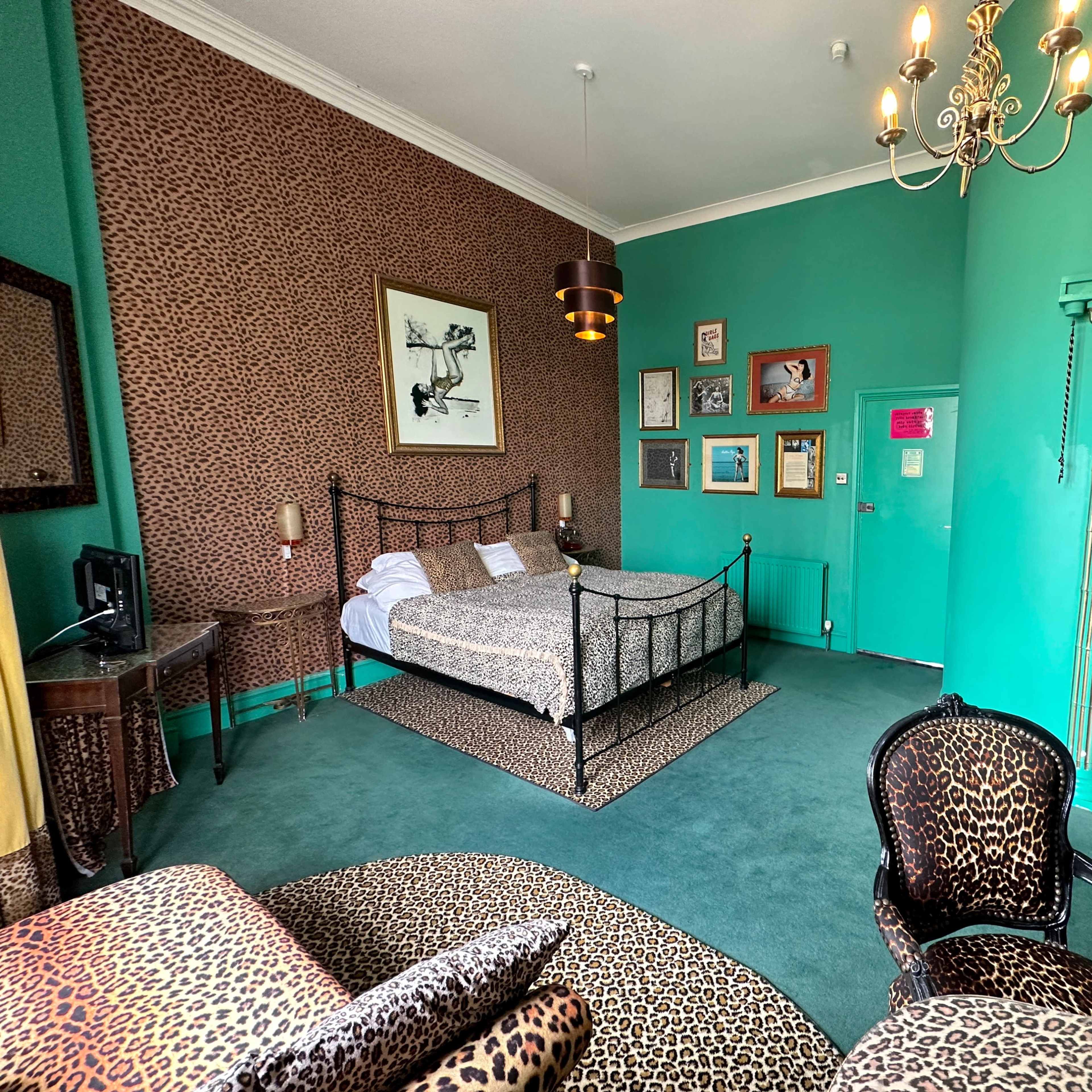 A room decorated with leopard-print furnishings, featuring a bed, a seating area, and vibrant teal walls.