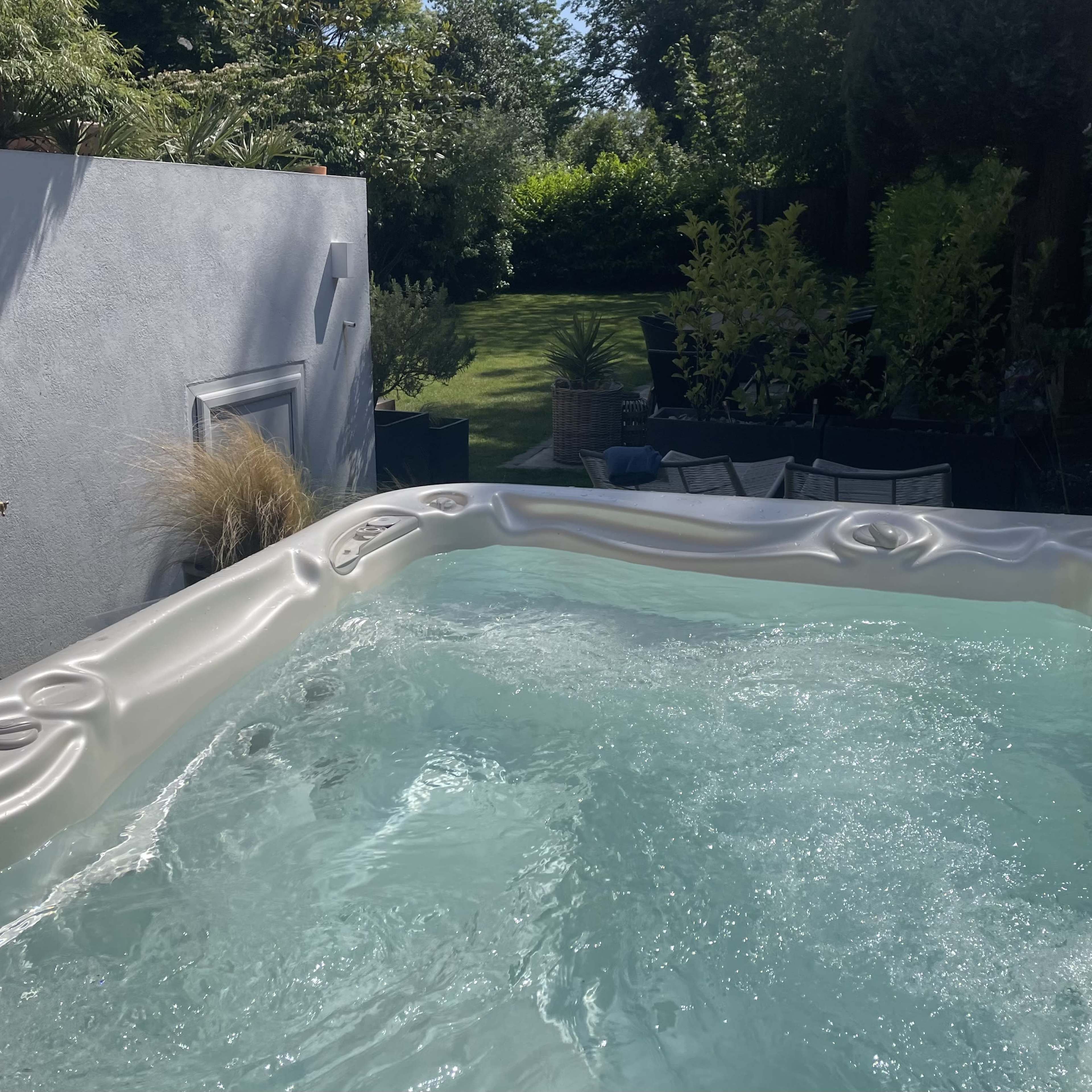 A hot tub with bubbling water, set against a backdrop of a green garden and patio furniture.