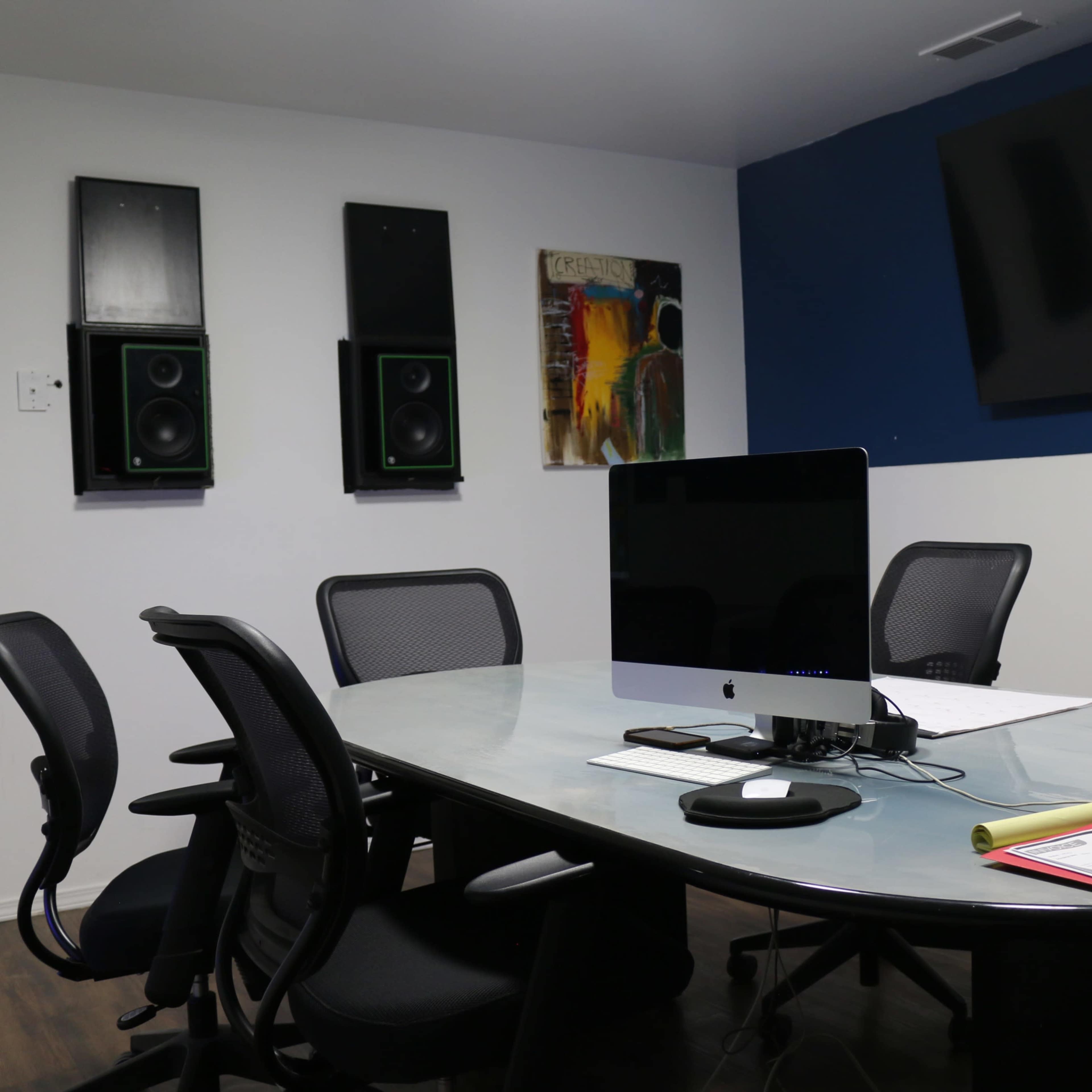 A conference room with a large oval table, several black office chairs, a computer monitor, and a laptop placed on the table, along with notes and documents on the surface.