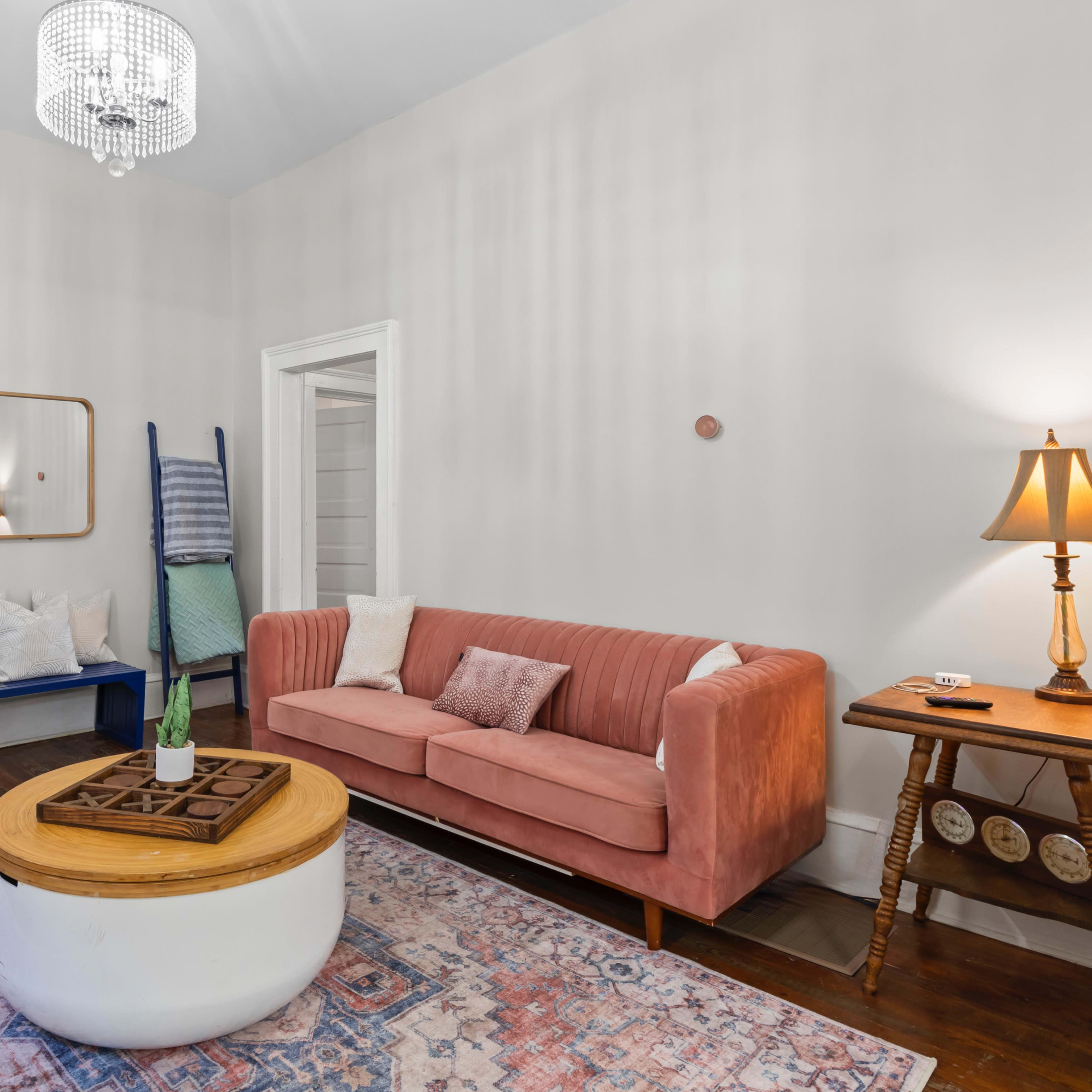 A neatly arranged living room with a pink sofa, a round coffee table, a patterned rug, and a chandelier overhead.