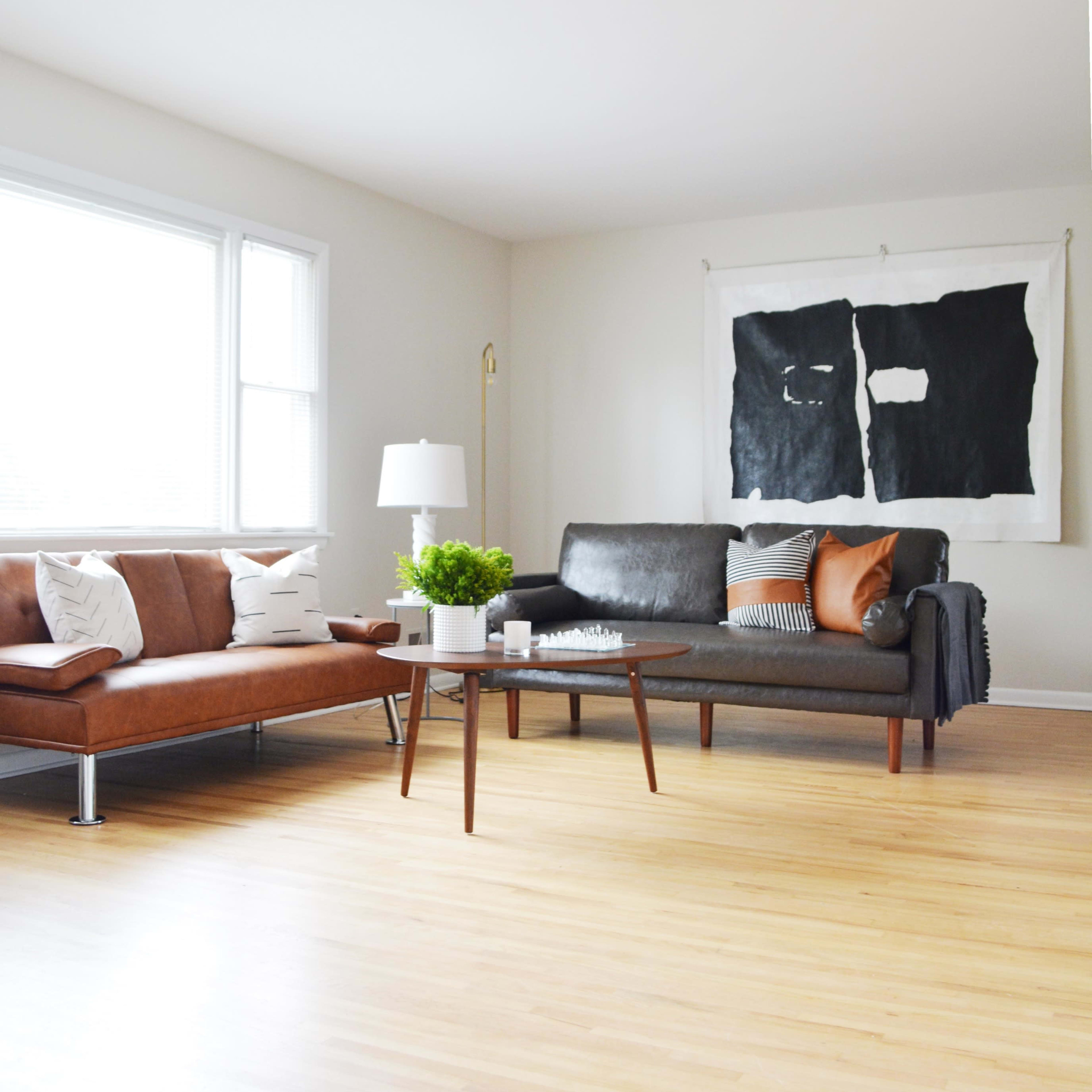A living room features a brown leather sofa and a black leather couch, accompanied by a coffee table and a large wall art piece.