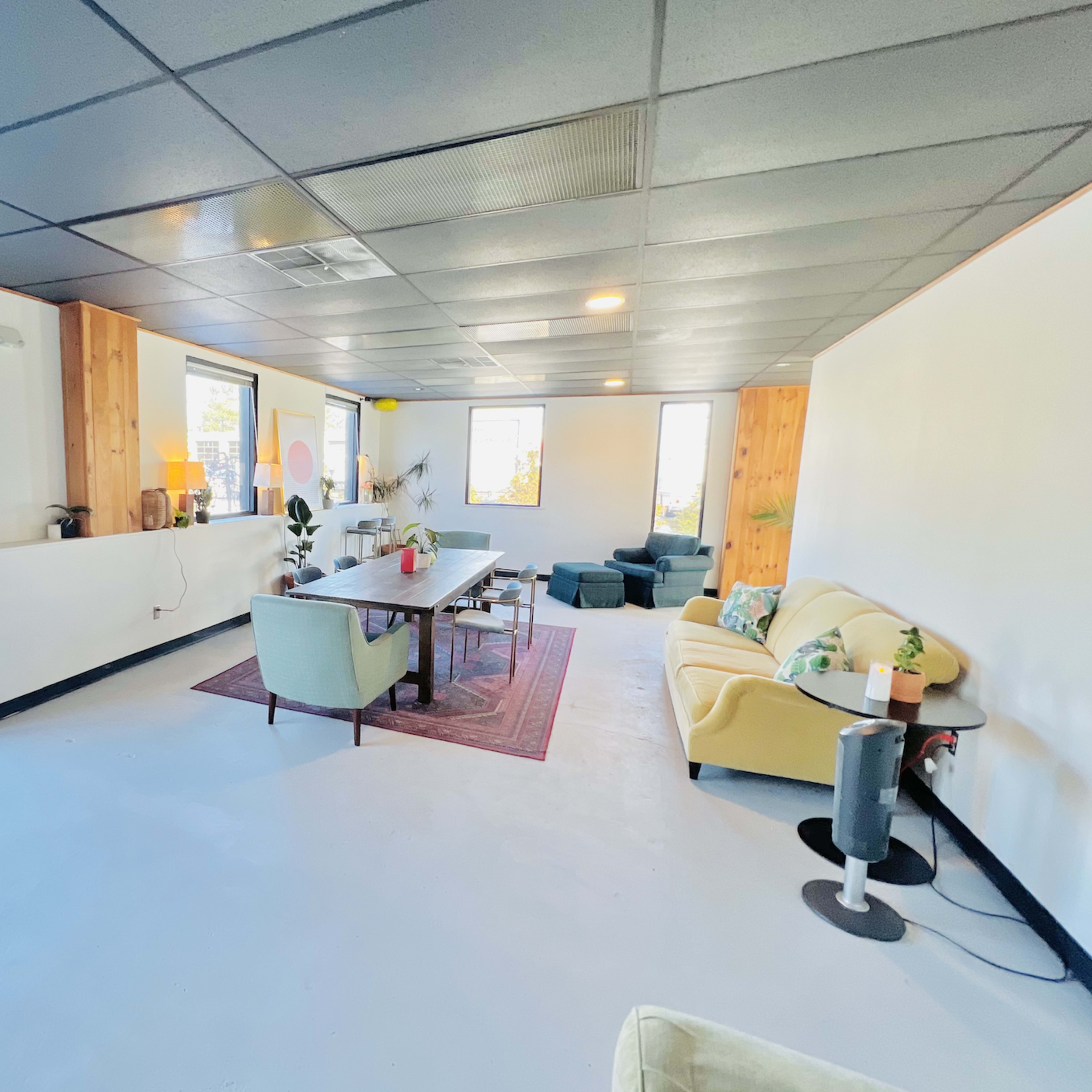 The room features a spacious, modern layout with a long dining table, various seating areas, and large windows allowing natural light to enter.