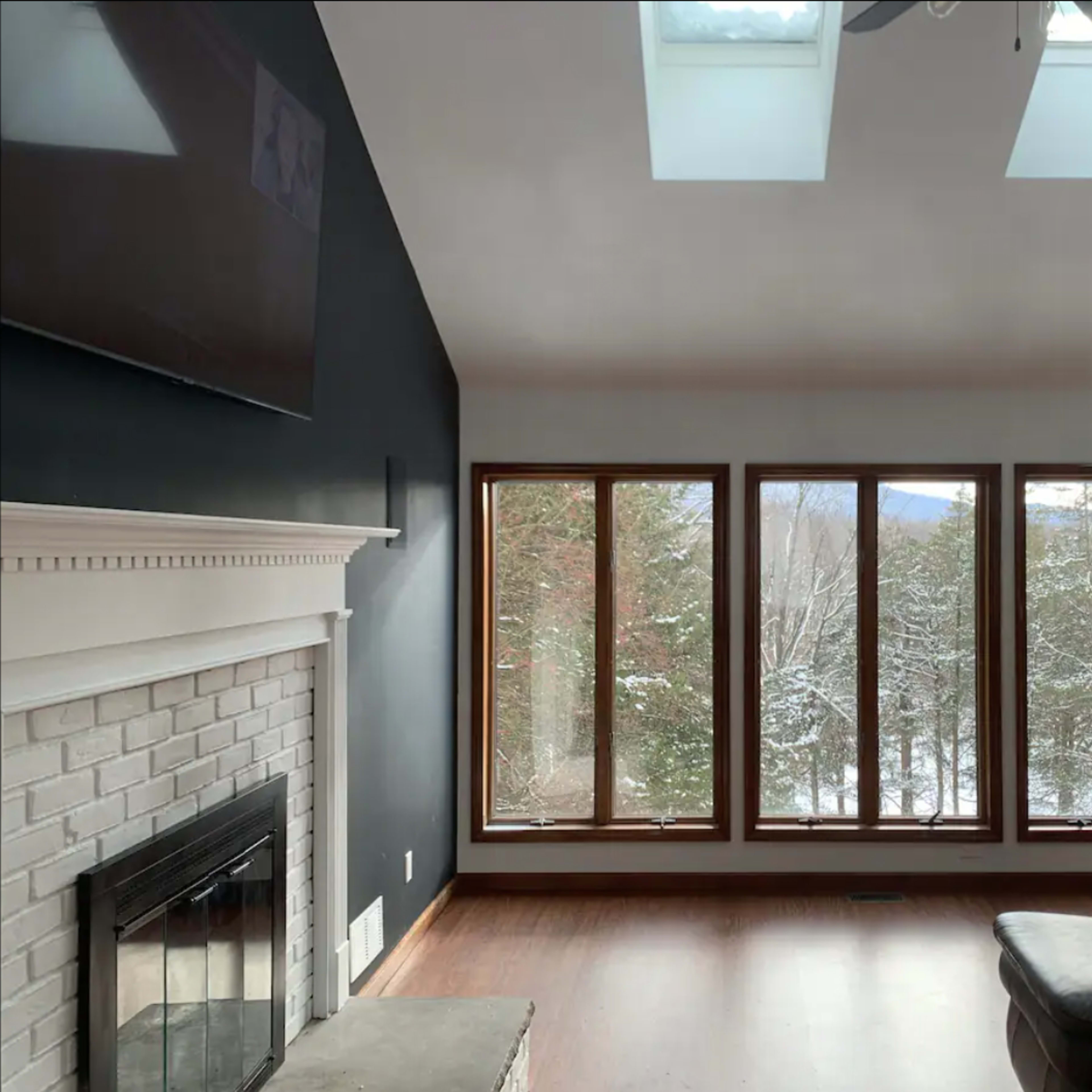 A living room features a brick fireplace and large windows overlooking a snowy outdoor landscape.