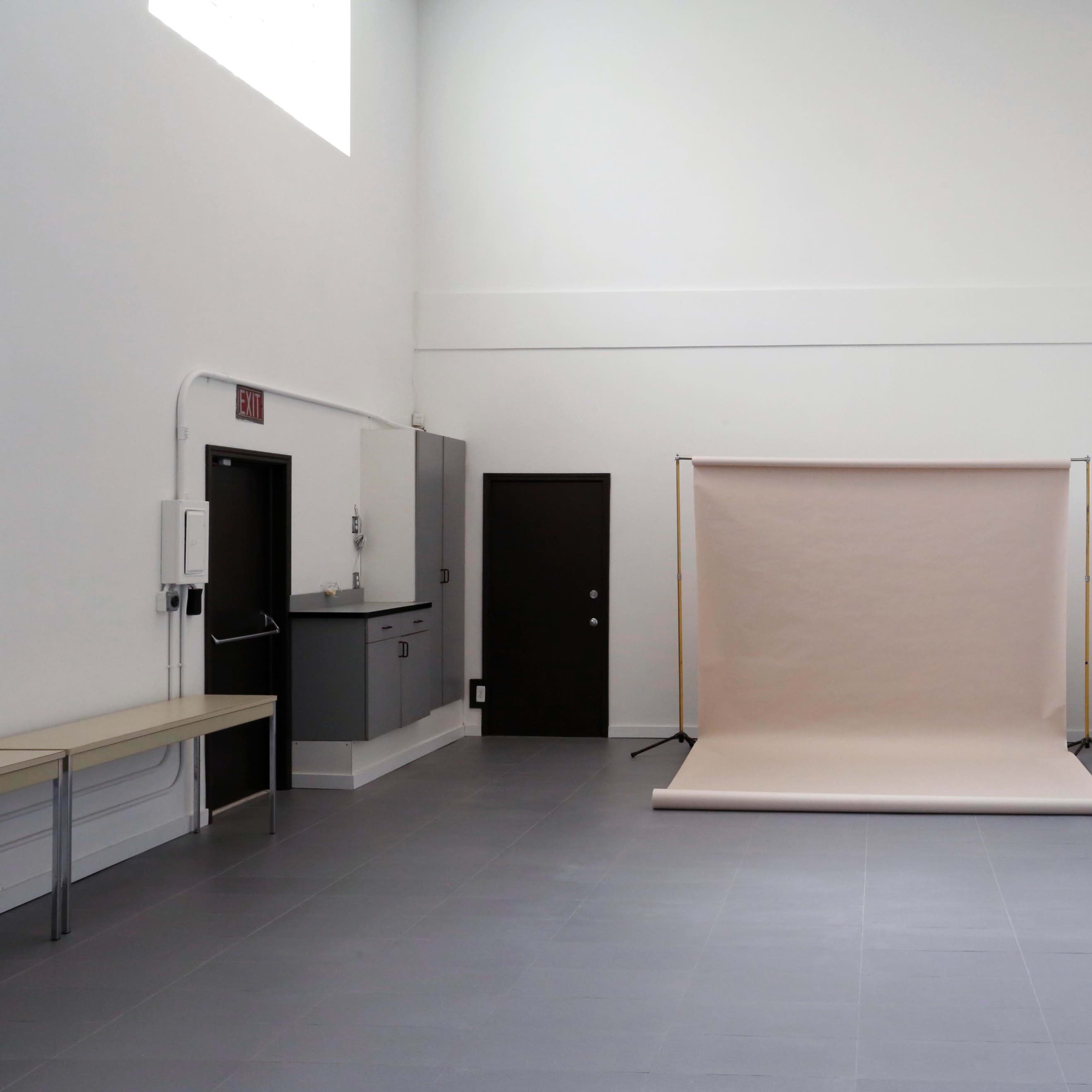 A spacious, minimalistic room with grey tiled flooring, a beige backdrop on a stand, and doors along the walls.