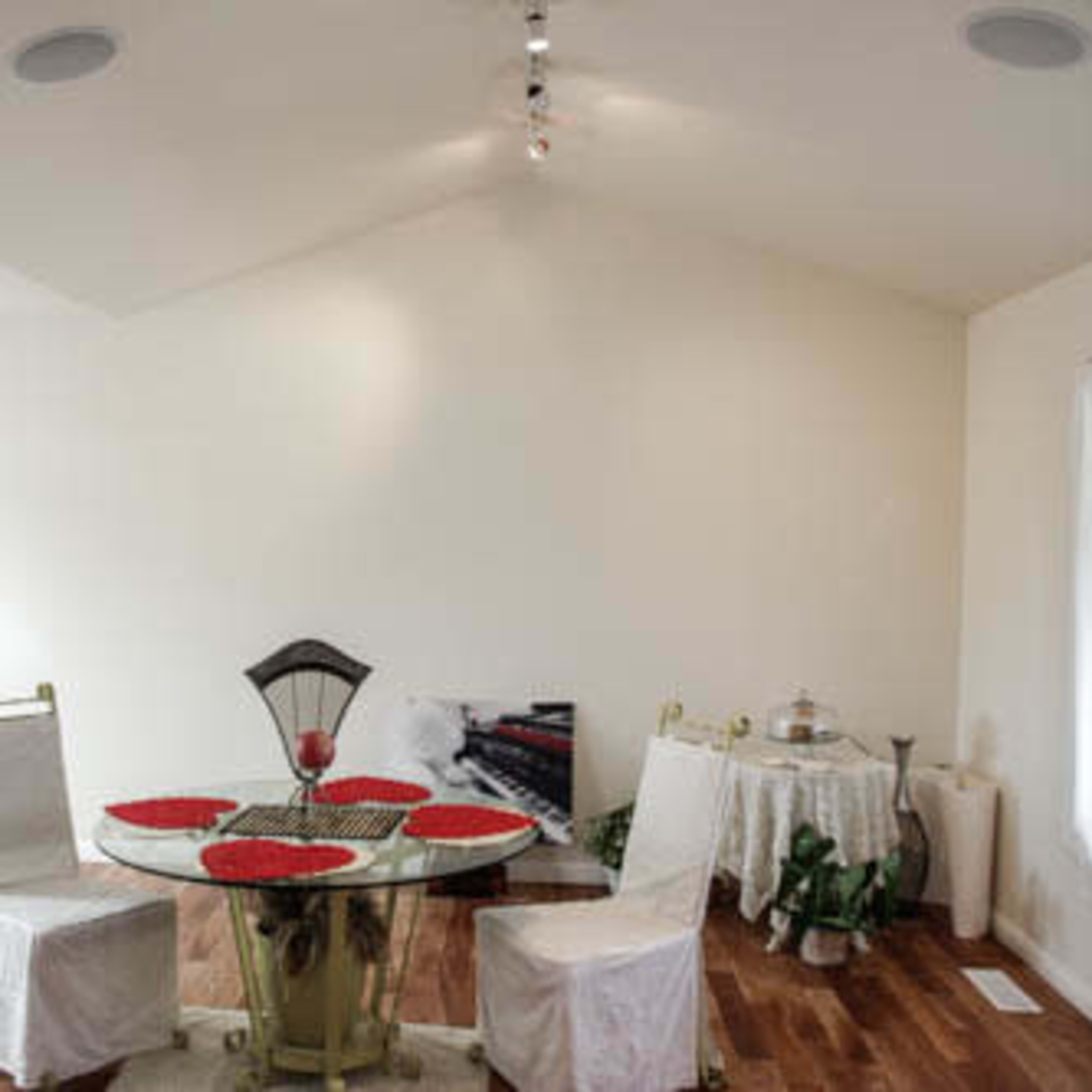 A dining area features a round table with red placemats and two chairs, surrounded by light-colored walls and hardwood flooring.