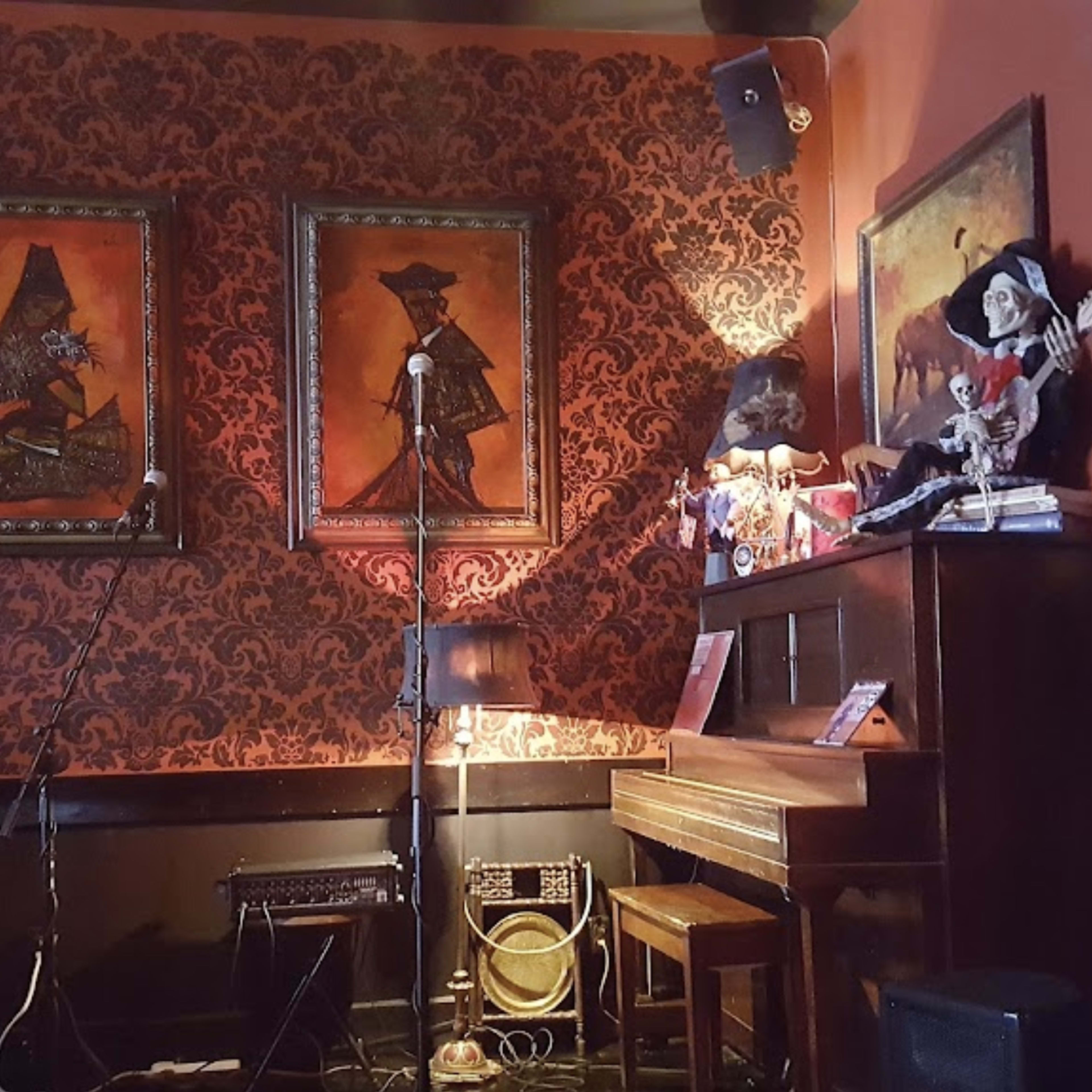 A corner of a bar with a piano, two framed paintings on the wall, and various decorations, including a microphone and musical equipment.