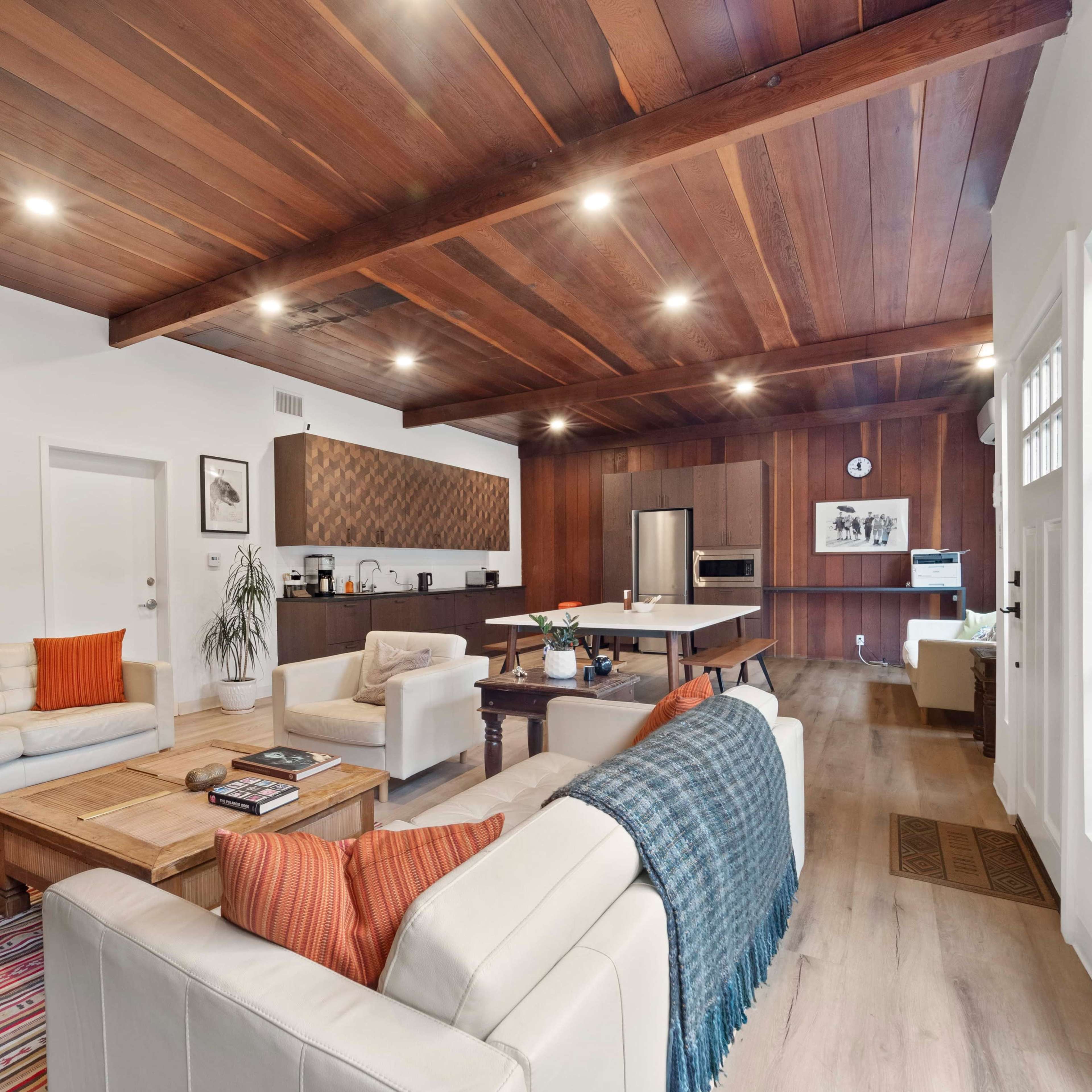 A spacious living area features a mix of wooden beams, modern furnishings, and a kitchen in the background.