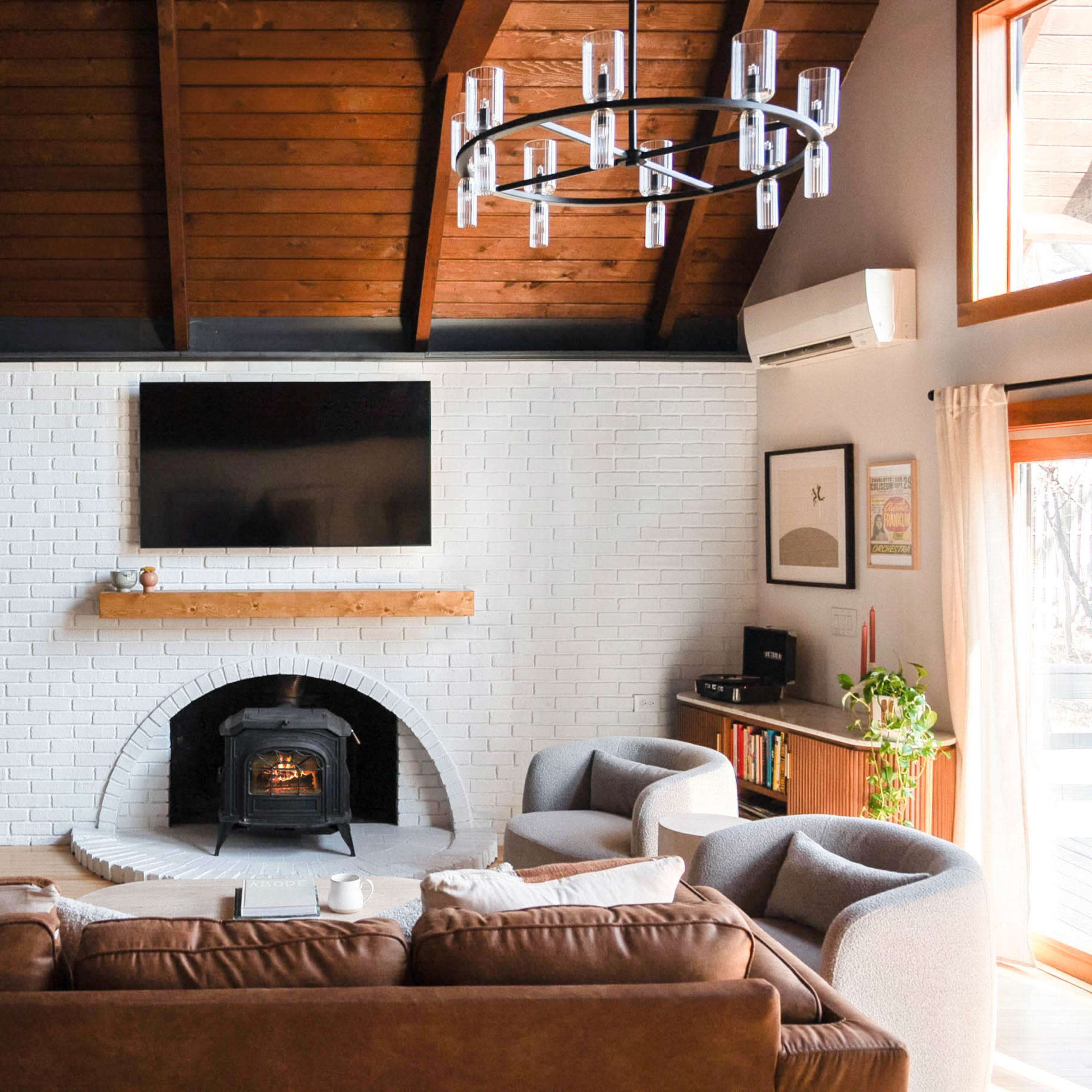 The living room features a white brick fireplace, a large flat-screen TV mounted above a wooden mantel, and a seating area with a brown sofa and gray armchairs.
