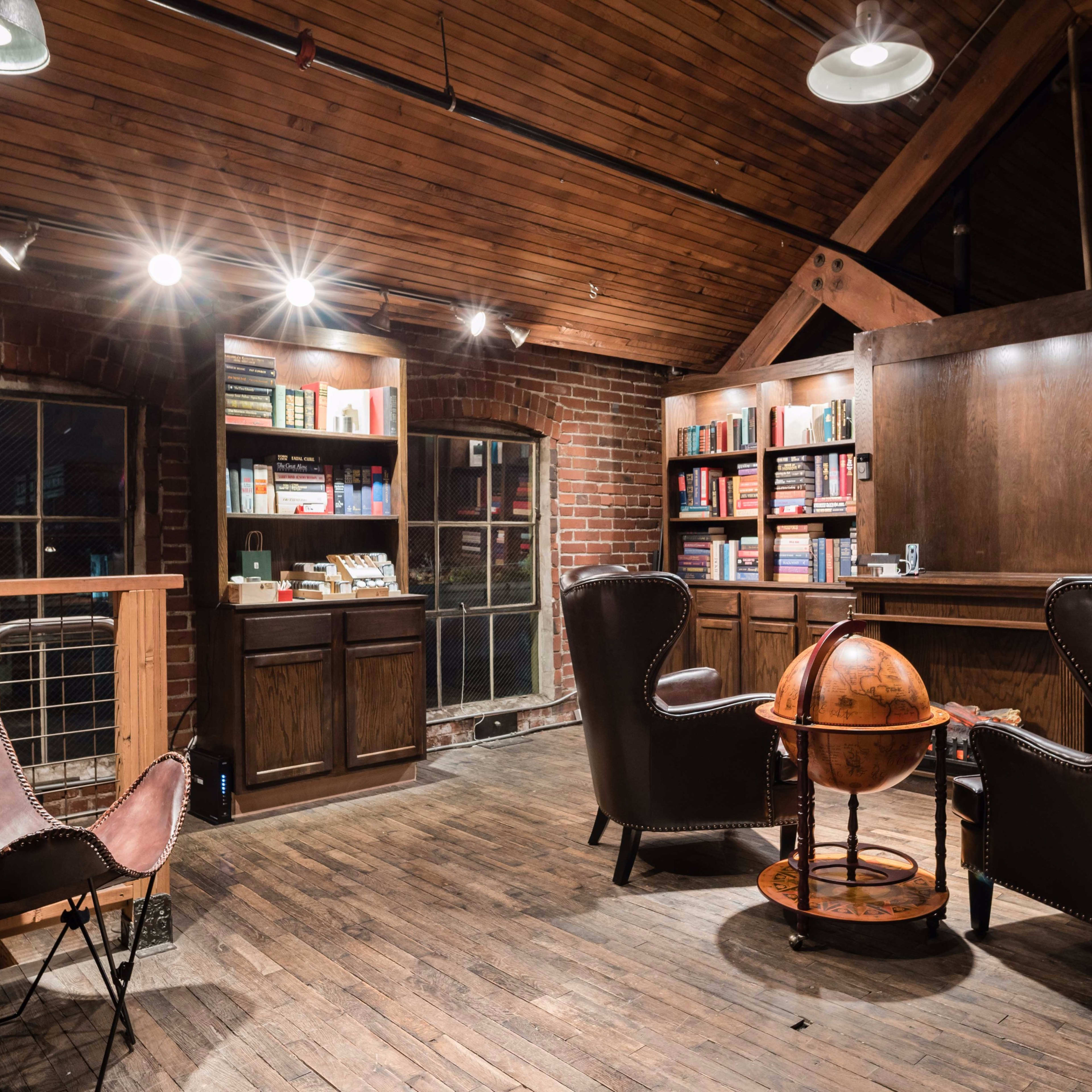 A warmly lit library with wooden shelves filled with books, two leather chairs, and a globe on a wooden table.