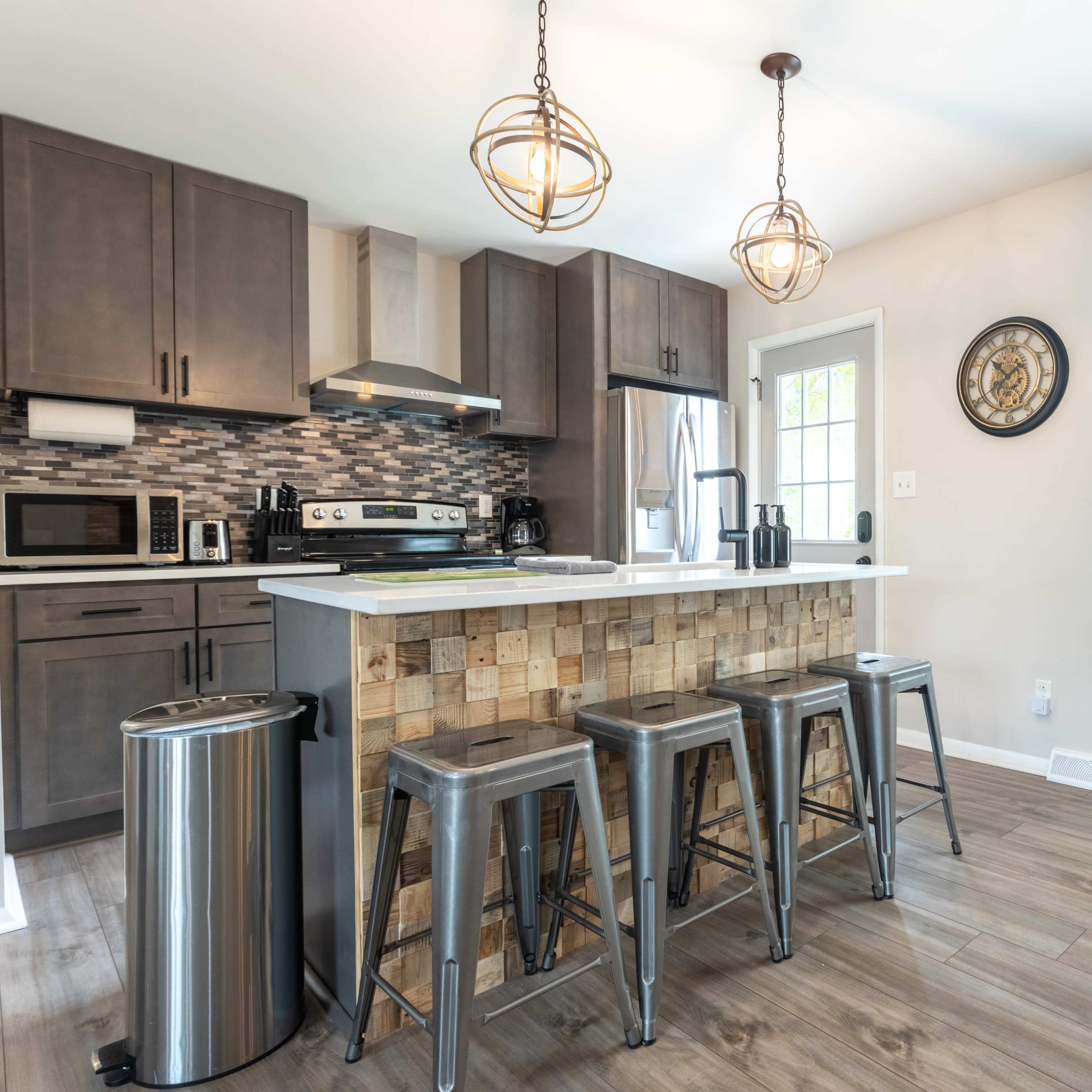 A modern kitchen features gray cabinetry, stainless steel appliances, and a wooden-paneled island with metal bar stools.