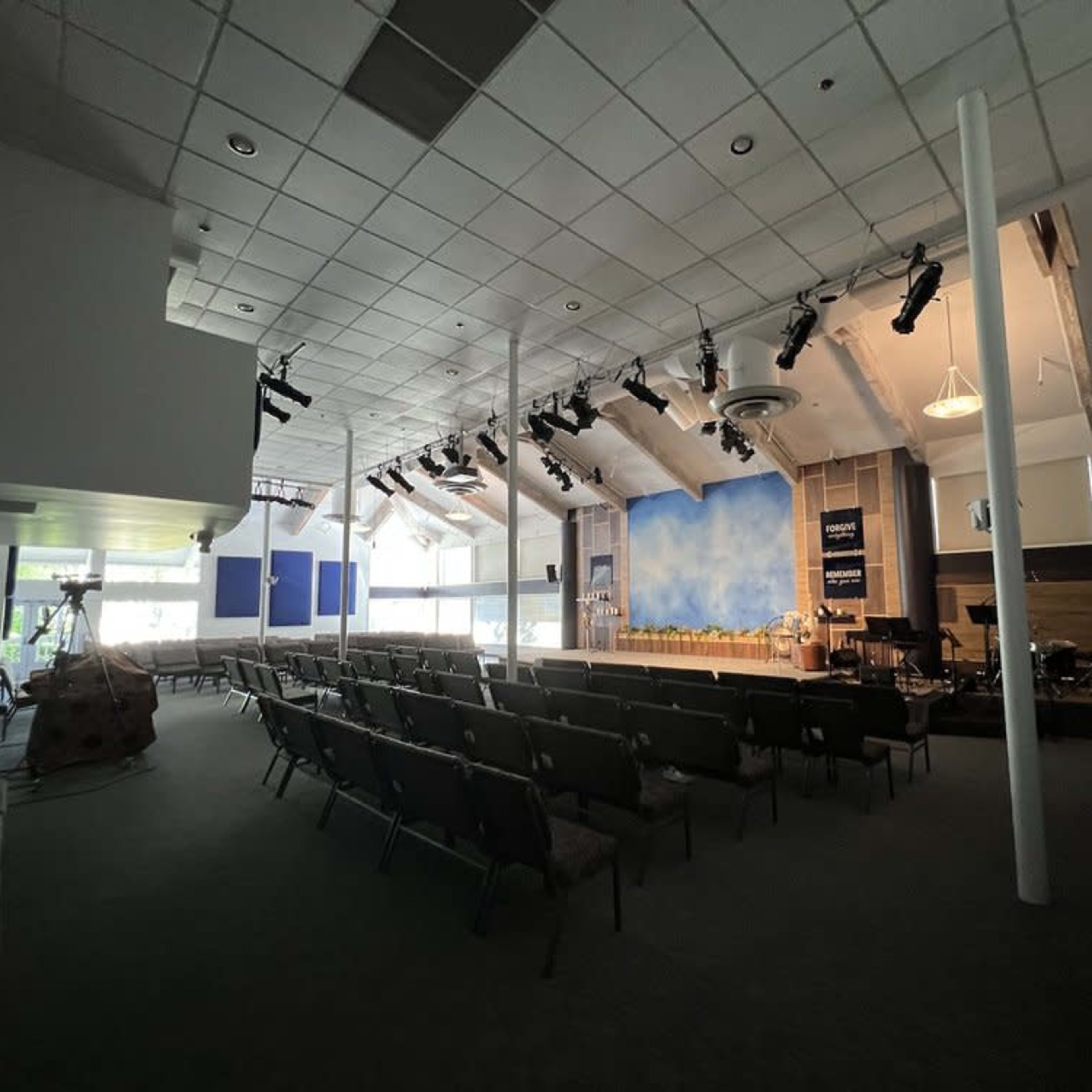 A spacious indoor auditorium with rows of chairs facing a stage, which features a blue backdrop and musical instruments set up.