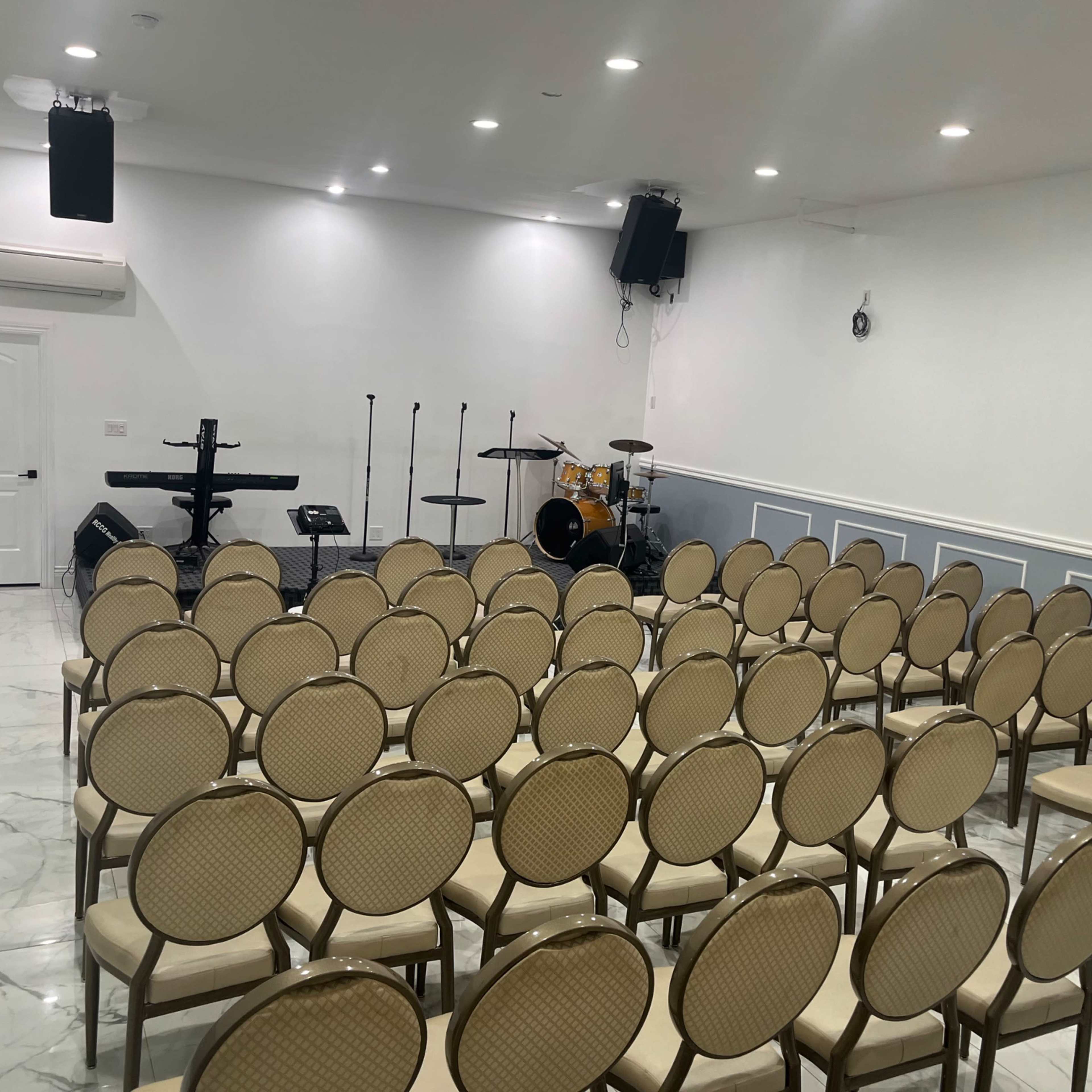 A well-arranged hall with rows of empty chairs facing a small stage that has musical instruments set up.