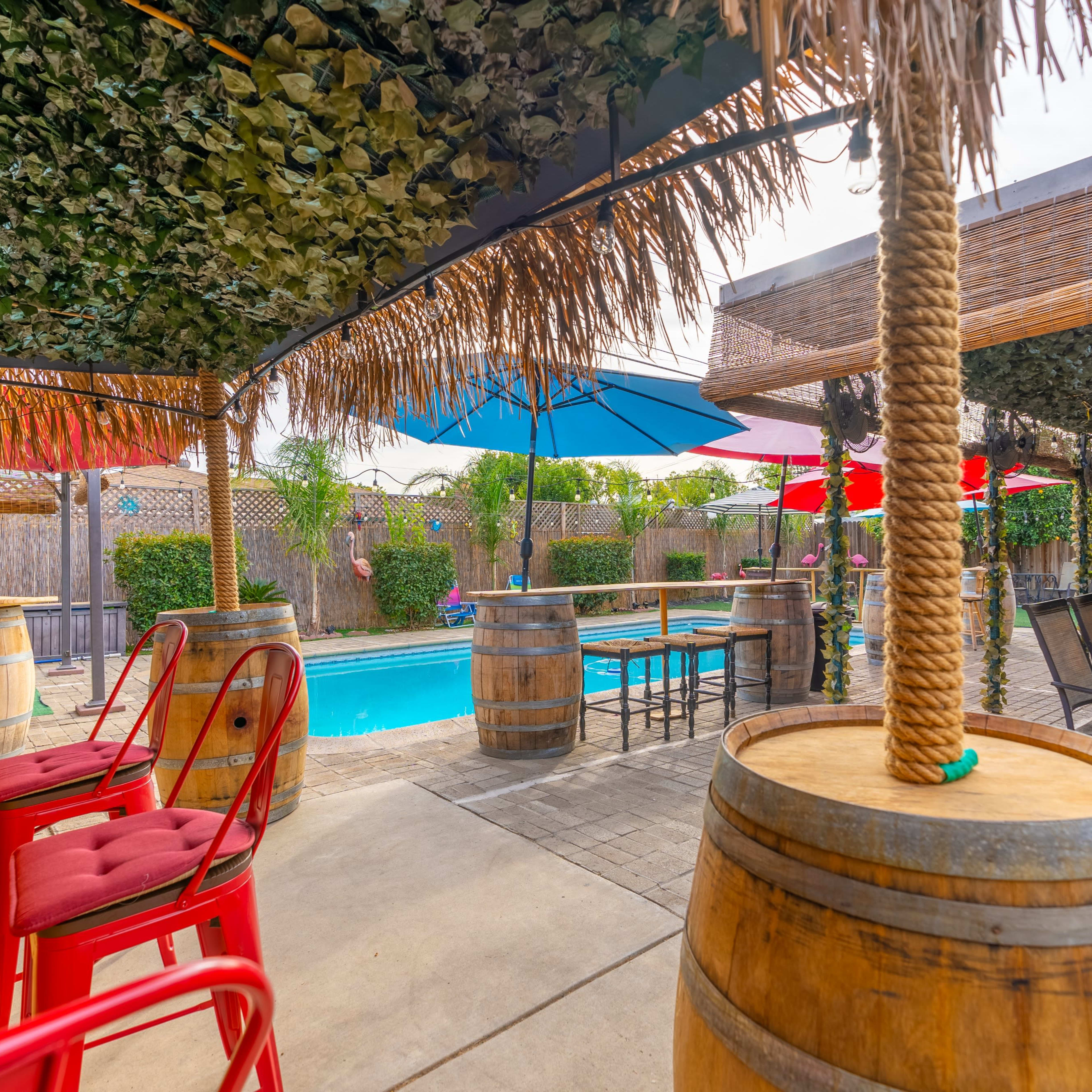 A poolside area with tropical-themed seating, a bar, and shaded umbrellas.
