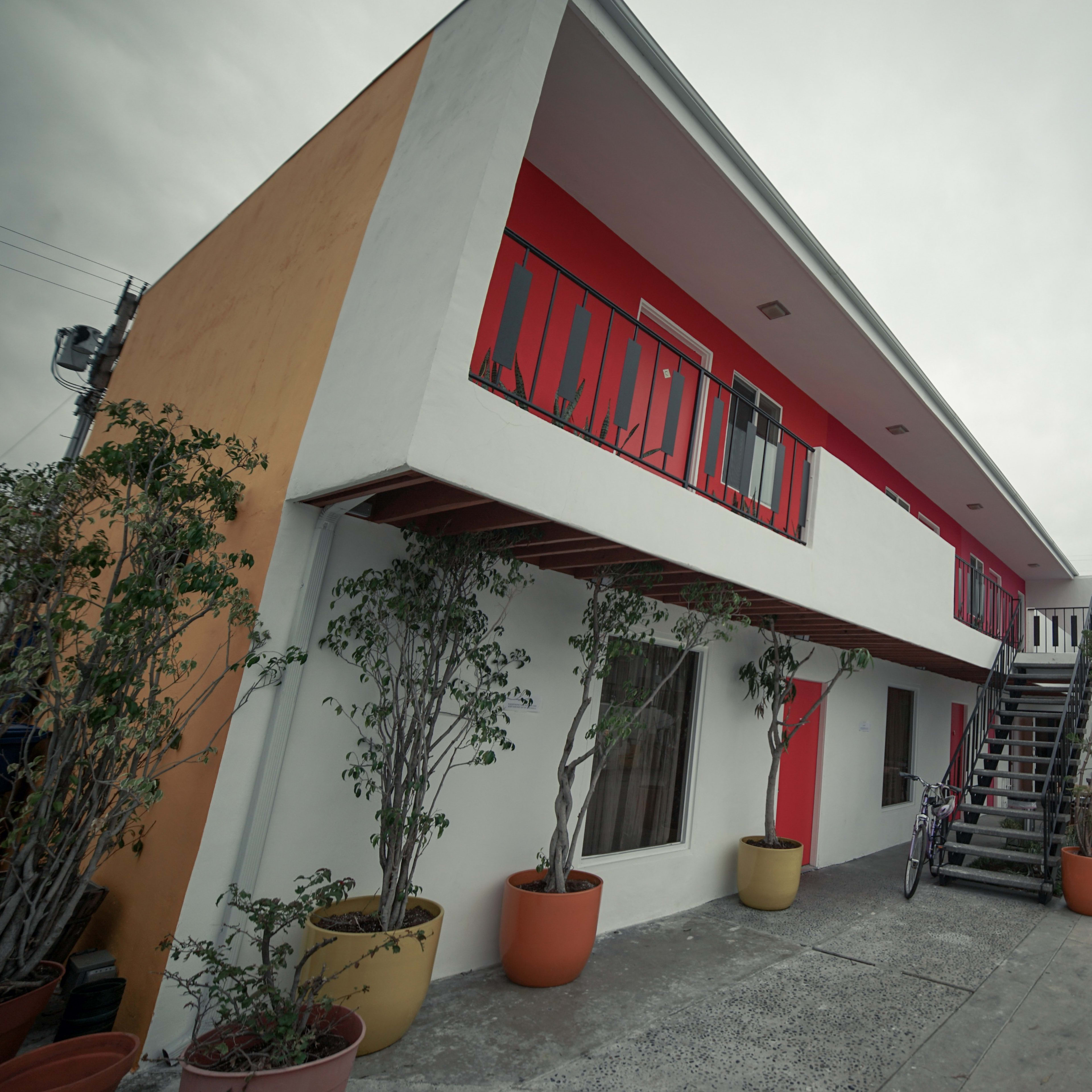 A two-story building with a red and white exterior, featuring potted plants and a staircase leading to the upper floor.