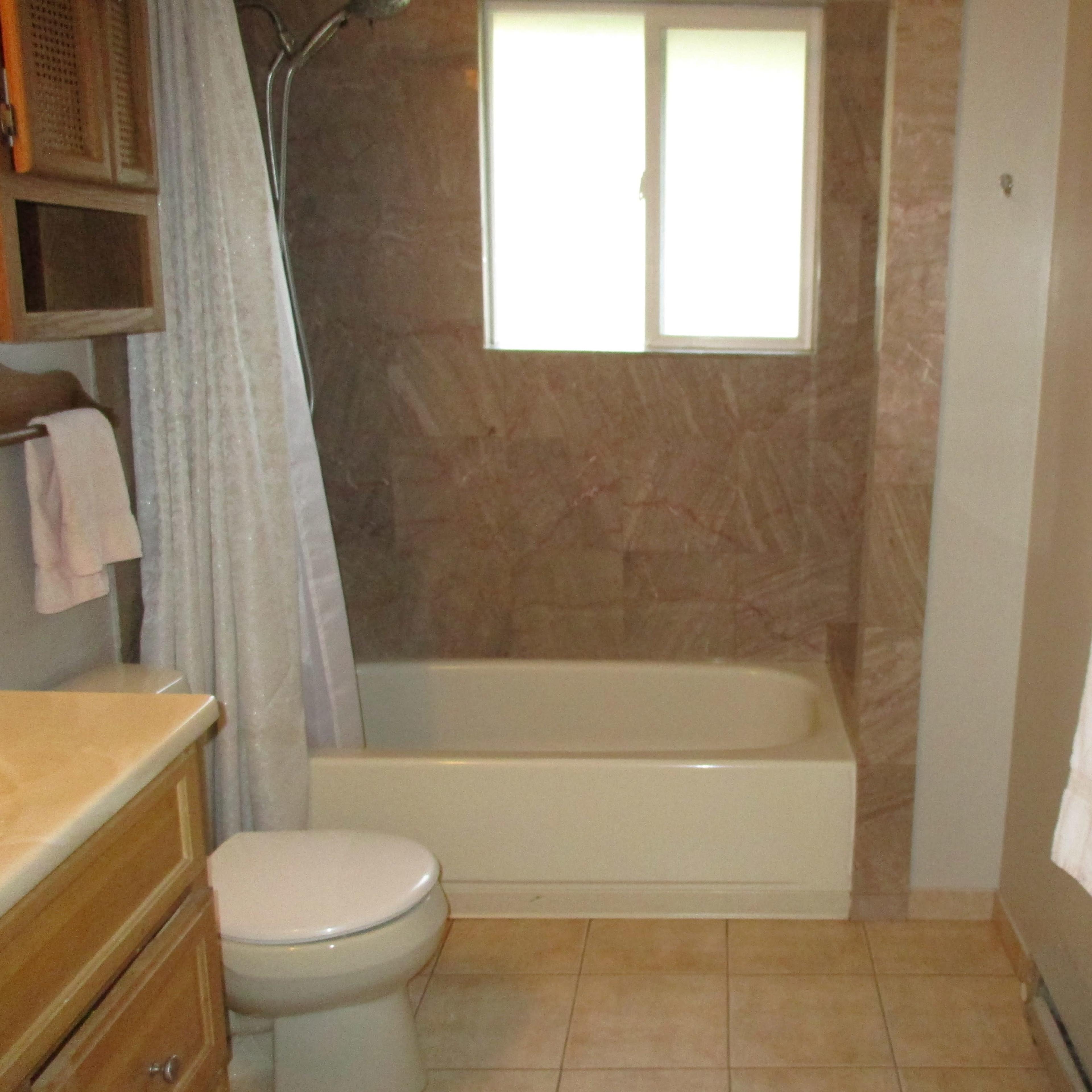 A bathroom with a tub and shower, a toilet, a sink with wooden cabinets, and towels hanging on a rack.
