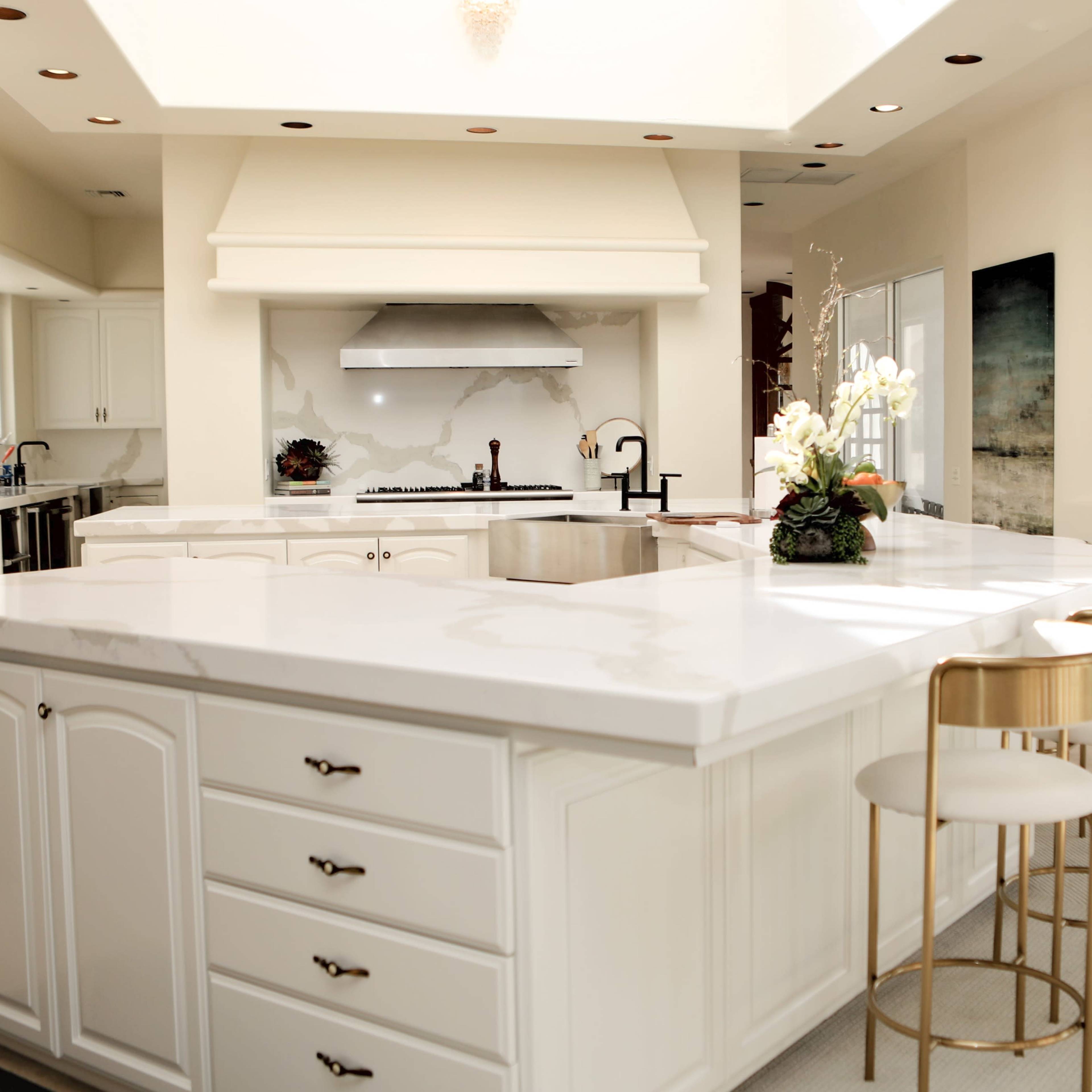 A modern kitchen featuring white cabinetry, a large island with a marble countertop, and gold-accented bar stools.