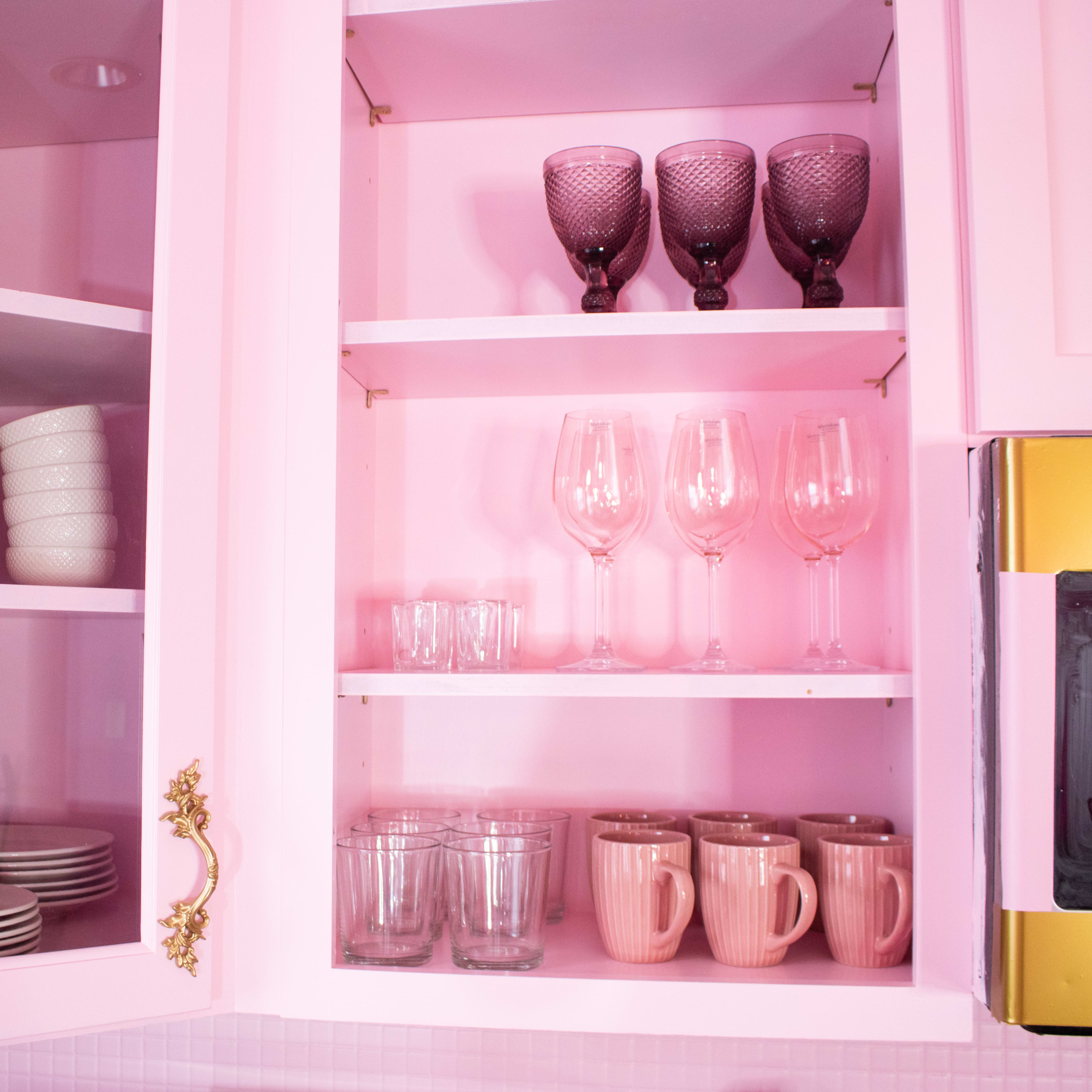 A pink cabinetry with various glassware, bowls, and cups arranged neatly on shelves.