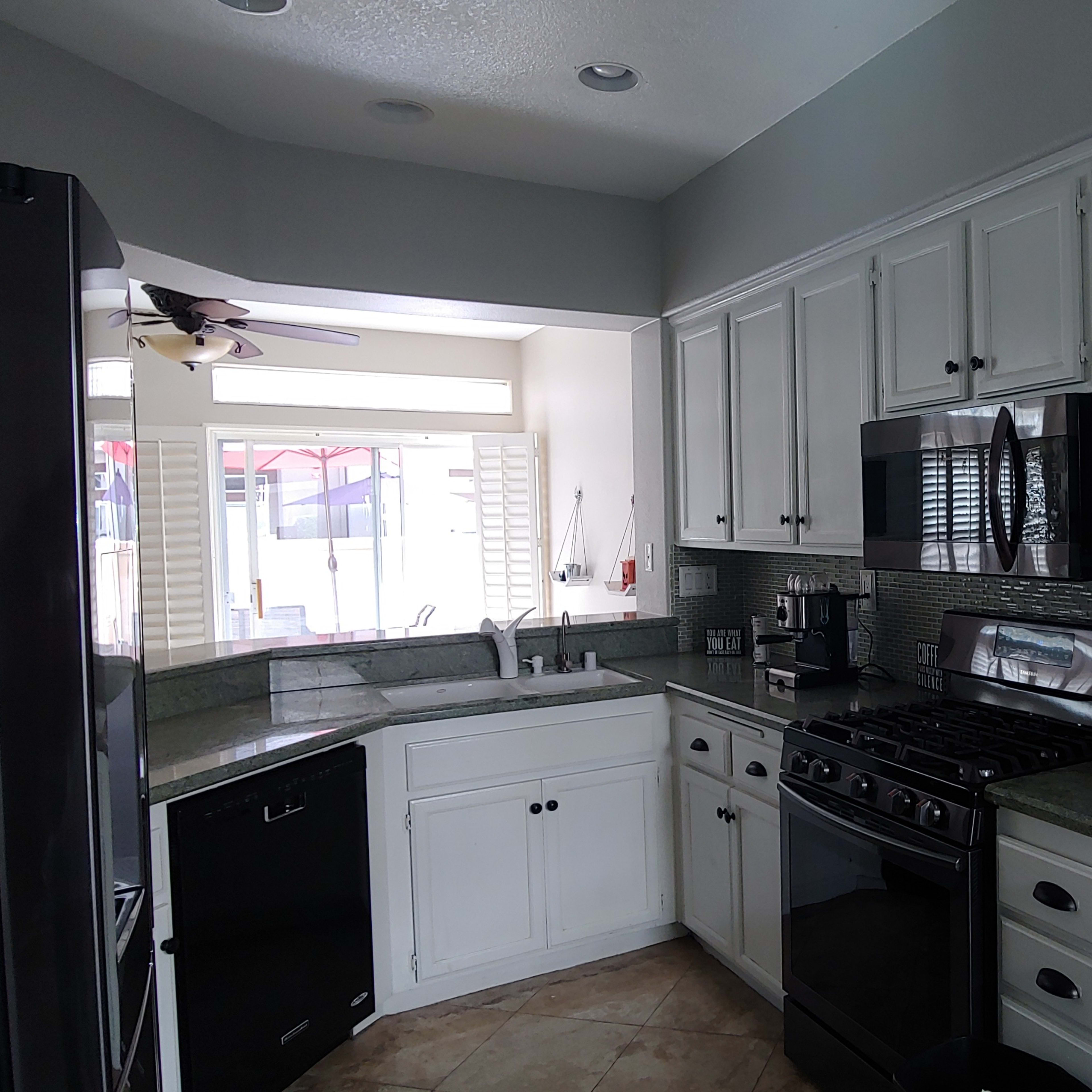 A modern kitchen with white cabinets, a black refrigerator, a stainless steel microwave, and a gas stove.
