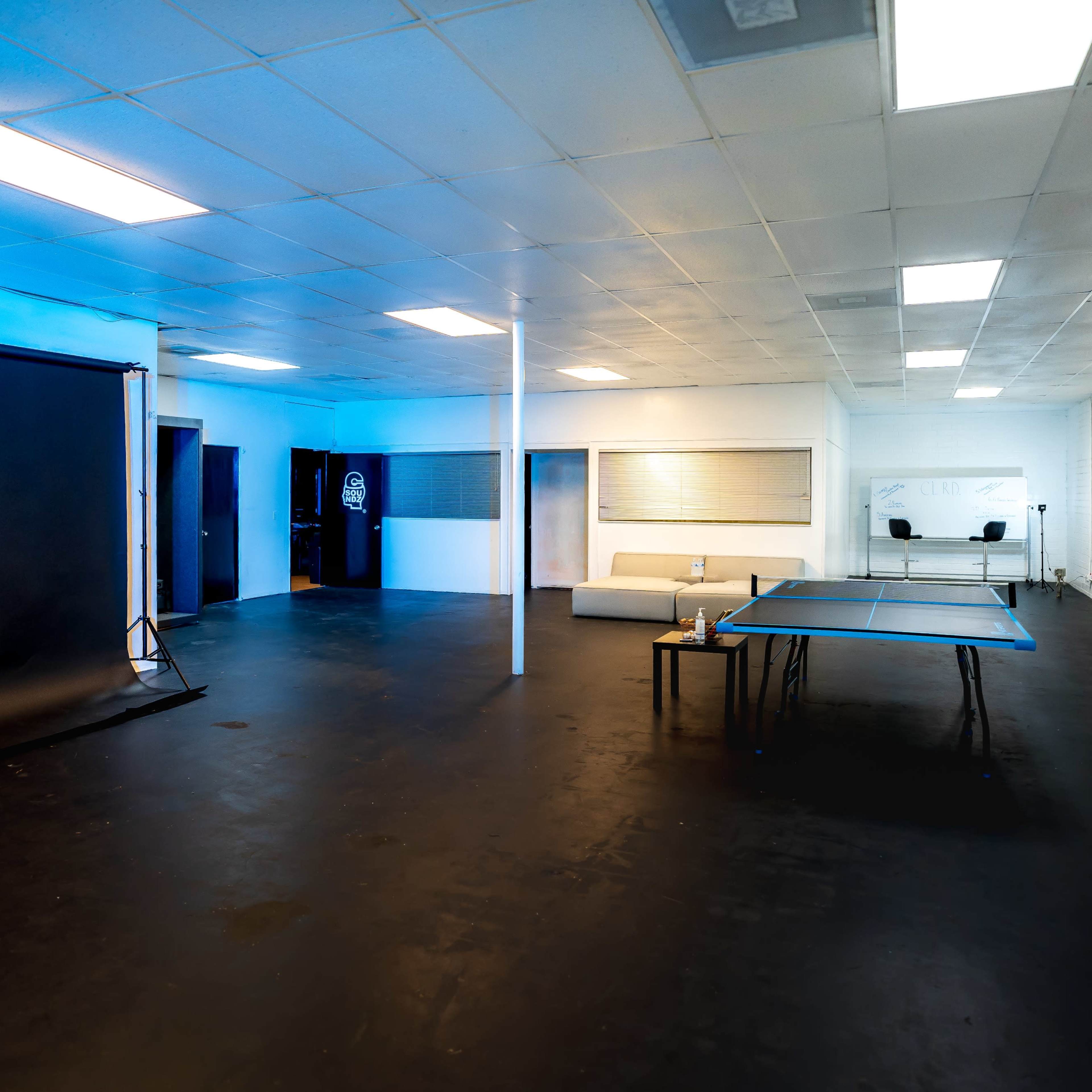 A spacious room with black flooring, featuring a black backdrop on a stand, a ping pong table, and a couch against the wall.