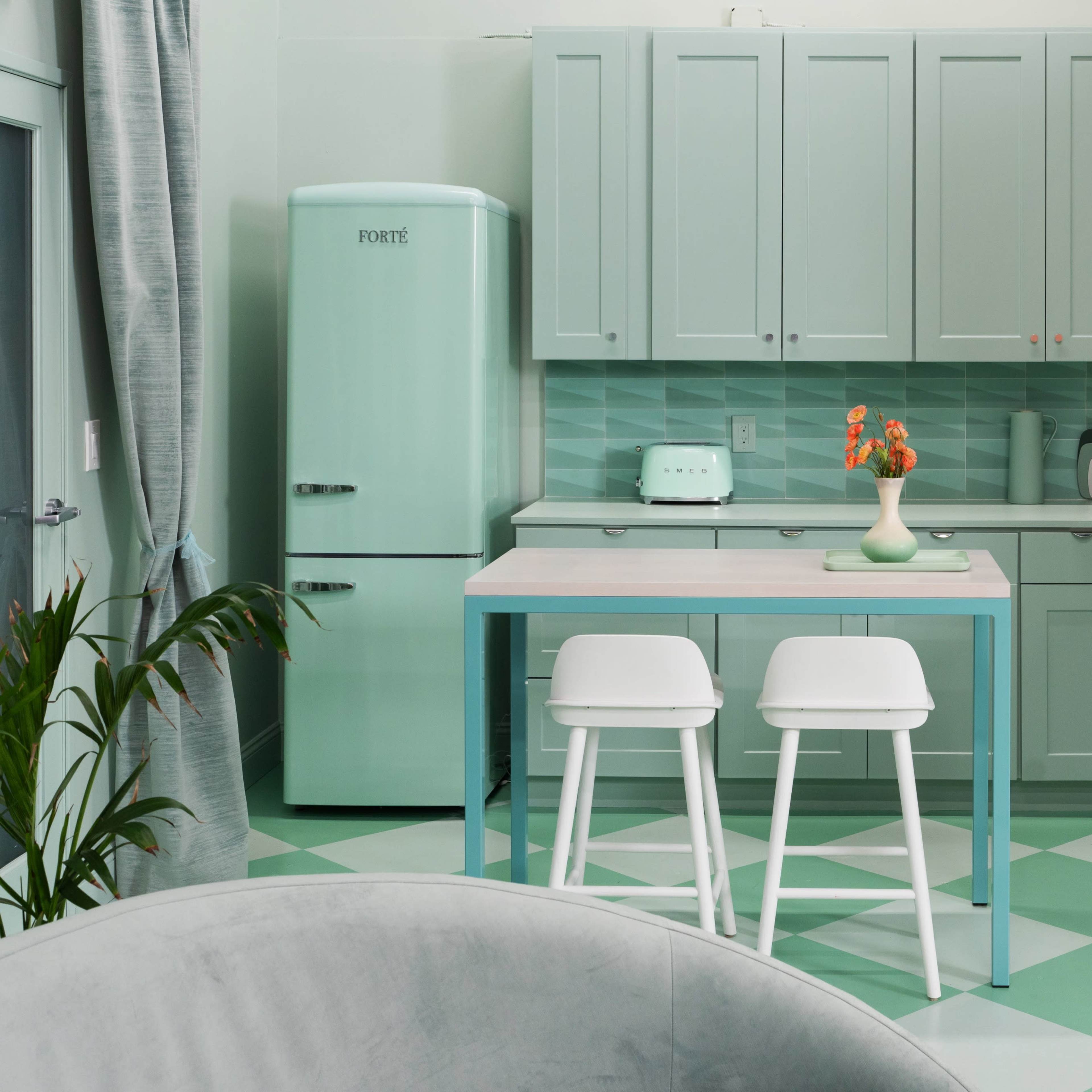 A modern kitchen featuring mint green cabinetry, a matching refrigerator, and a light-colored table with two stools.