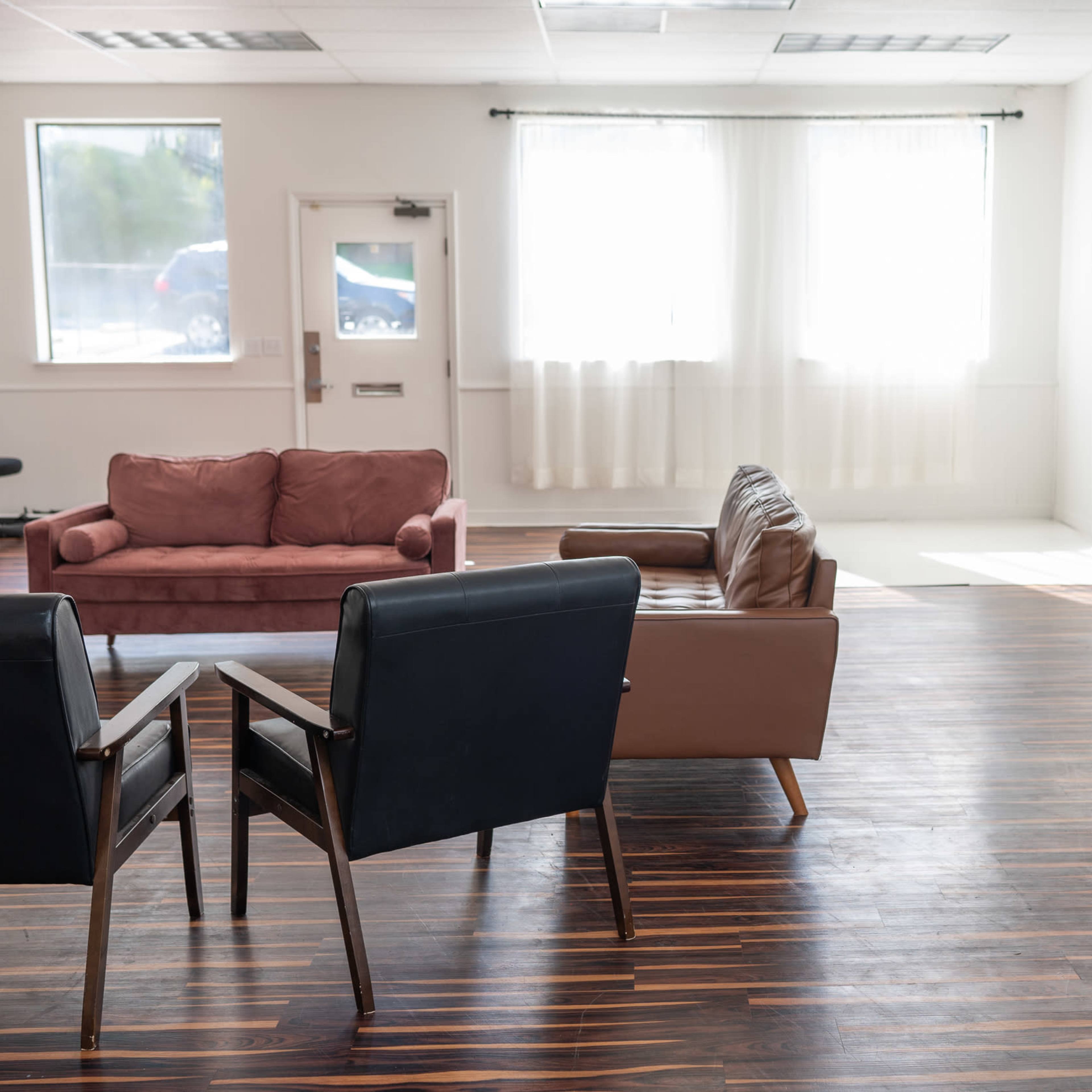 A spacious room with two sofas, a table, and a window letting in natural light, along with wooden flooring and minimal furnishings.