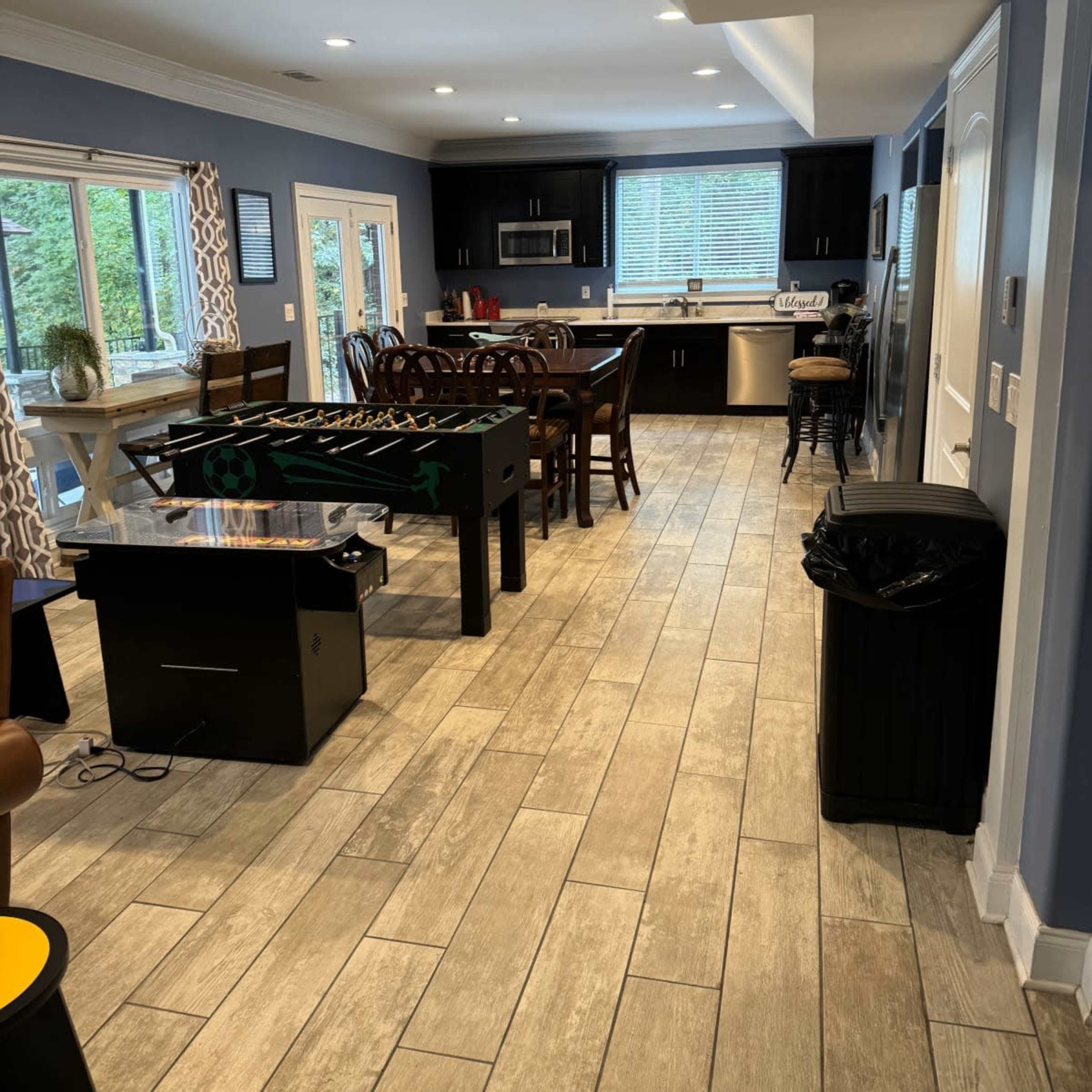 A spacious kitchen and dining area featuring dark cabinets, a wooden dining table, and a foosball table.