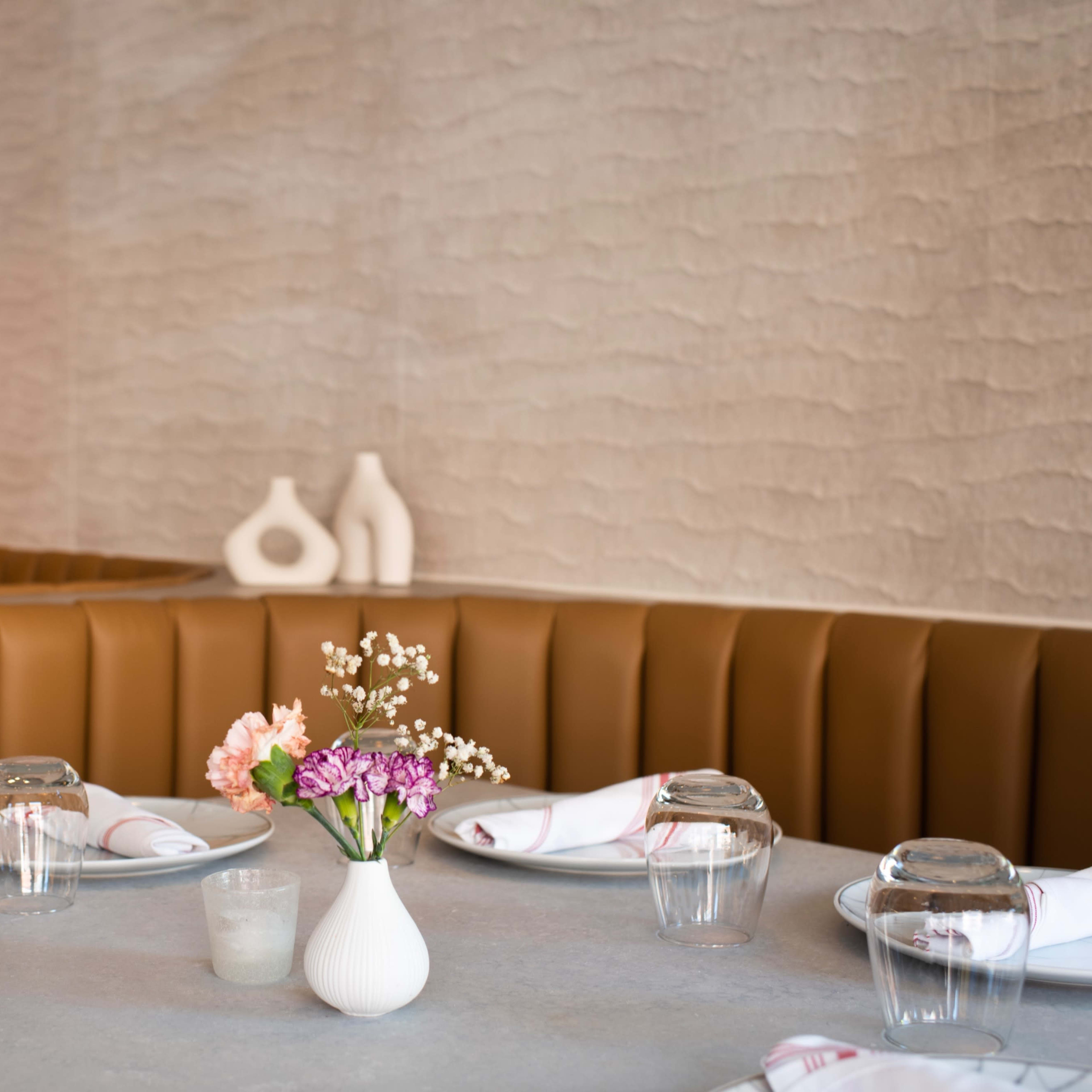 A modern restaurant interior with brown leather seating, a grey table, and a small vase of flowers as the centerpiece.
