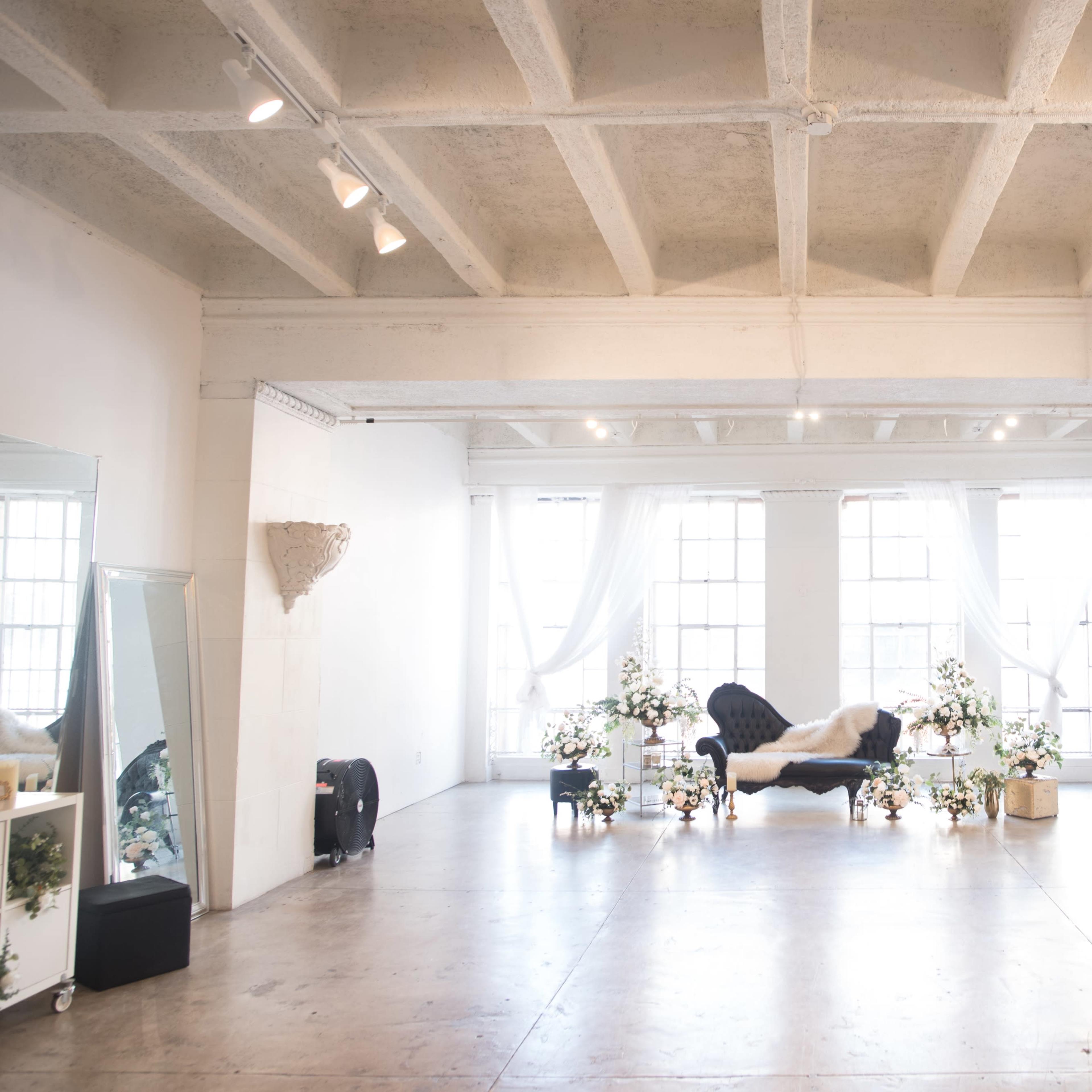 A spacious room with large windows, a navy blue sofa at the center, and decorative plants arranged around it.