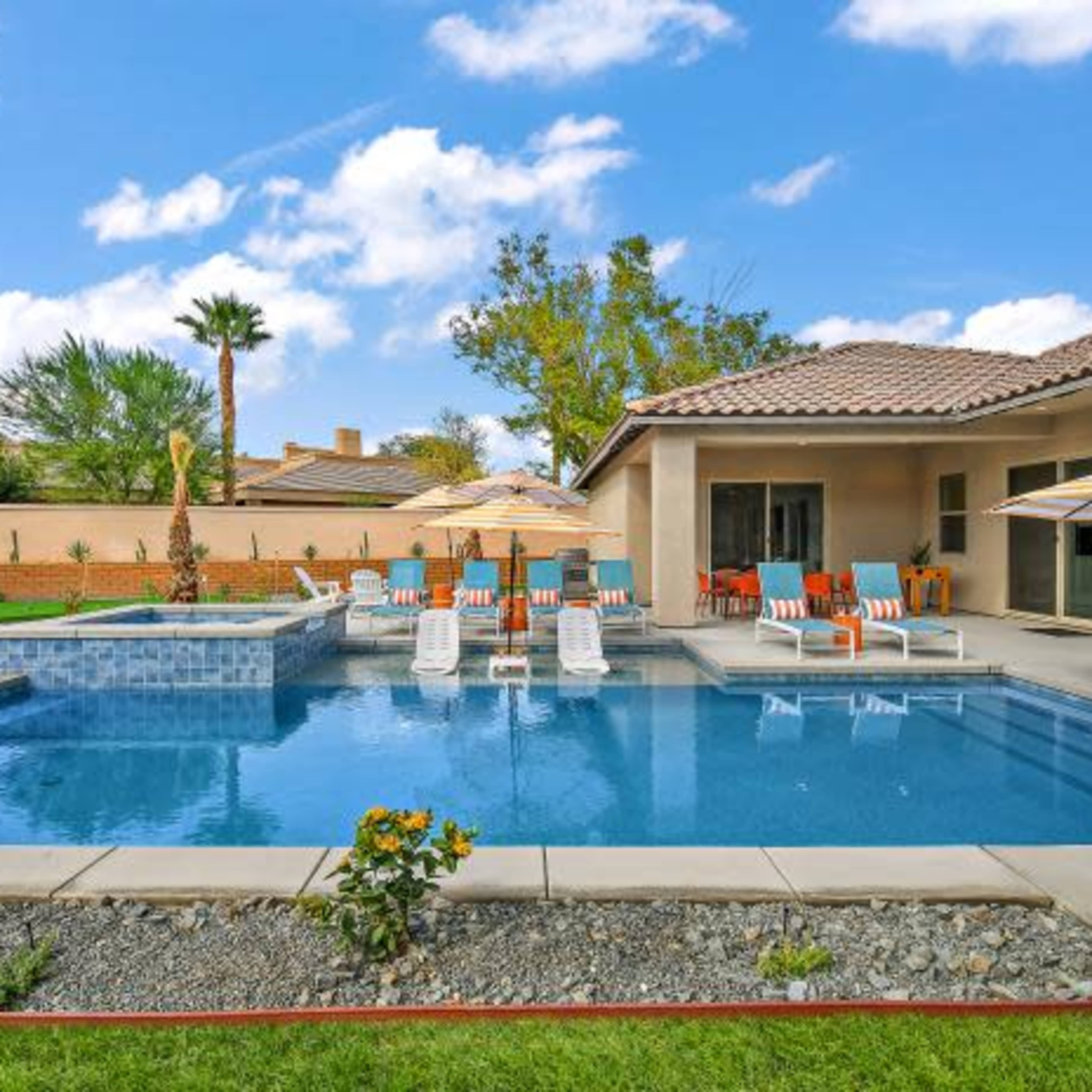 A backyard with a swimming pool, lounge chairs, umbrellas, and a landscaped garden.