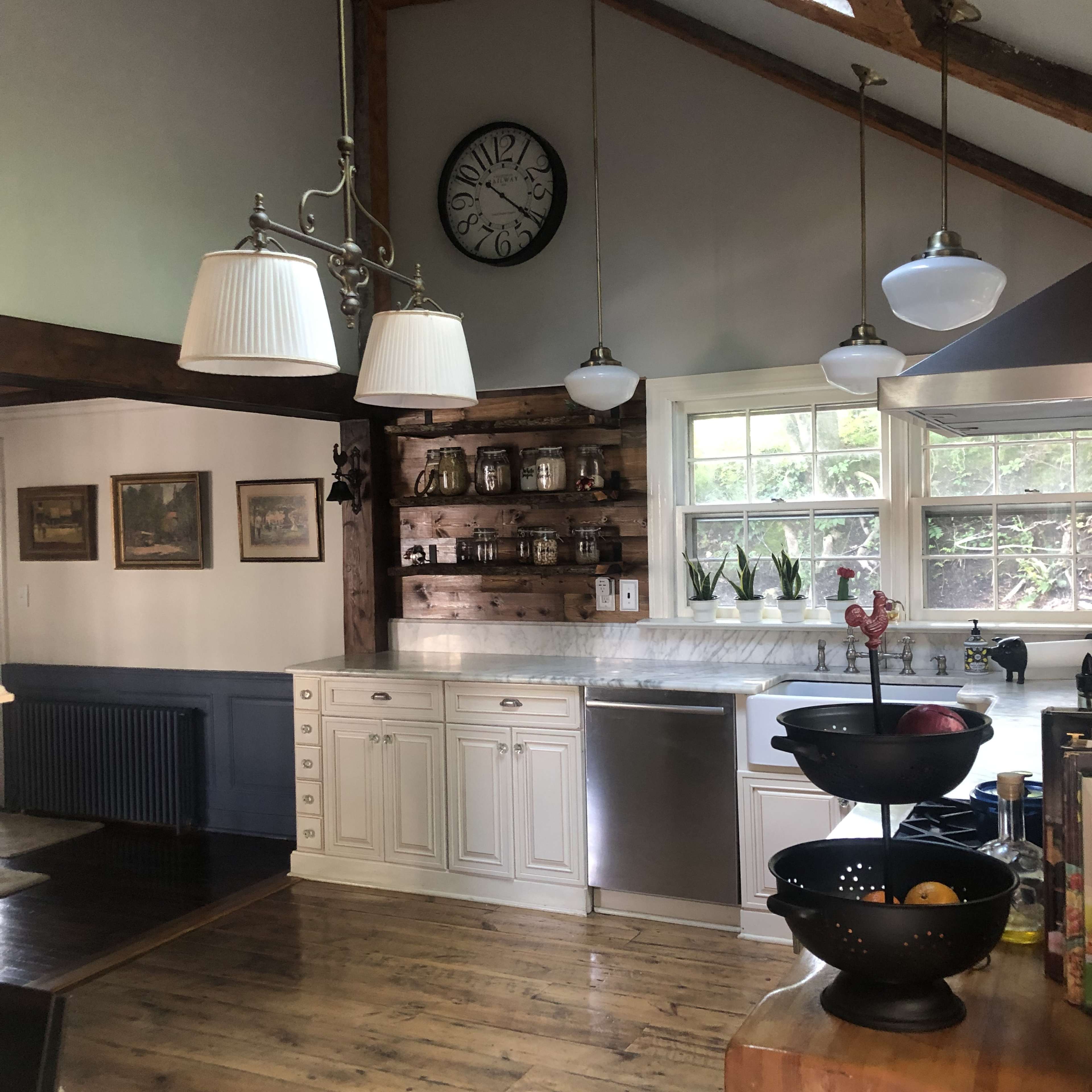 A bright kitchen with white cabinetry, a stone countertop, and a clock on the wall, featuring a mix of modern and rustic elements.