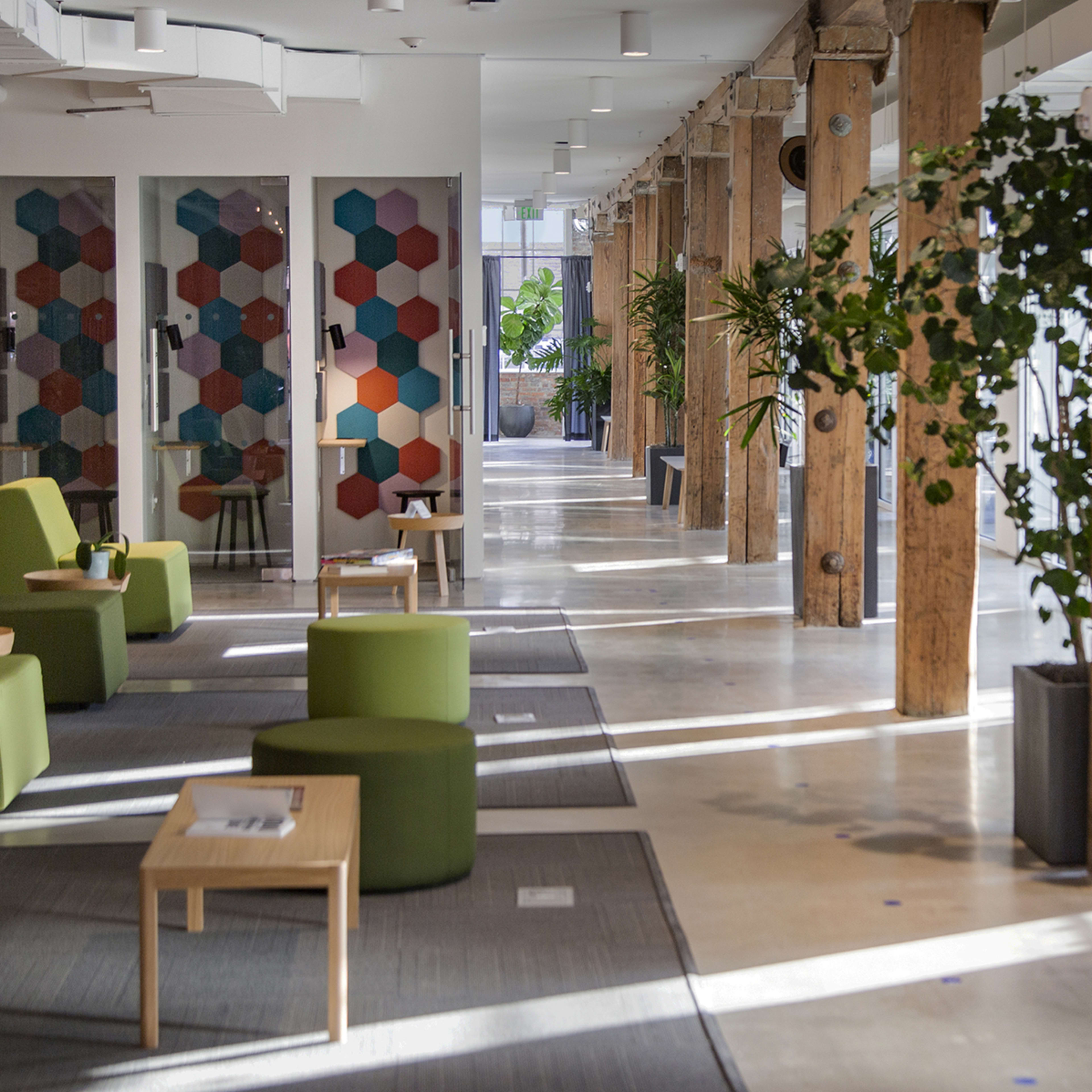A corridor with green seating arrangements and wooden pillars, featuring plants and decorative panels along the walls.