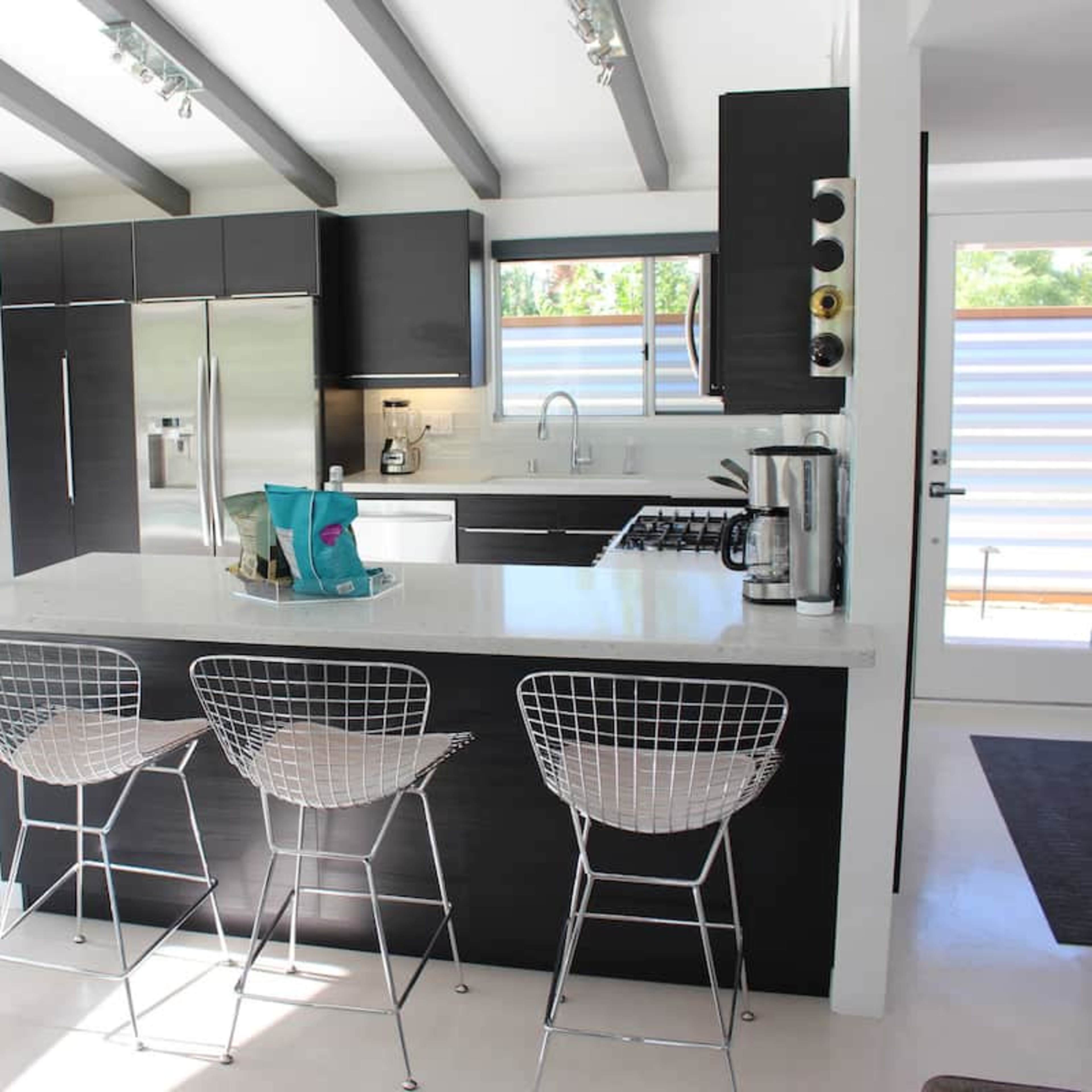 A modern kitchen with a black cabinetry, a white countertop, and three wire bar stools positioned at a central island.