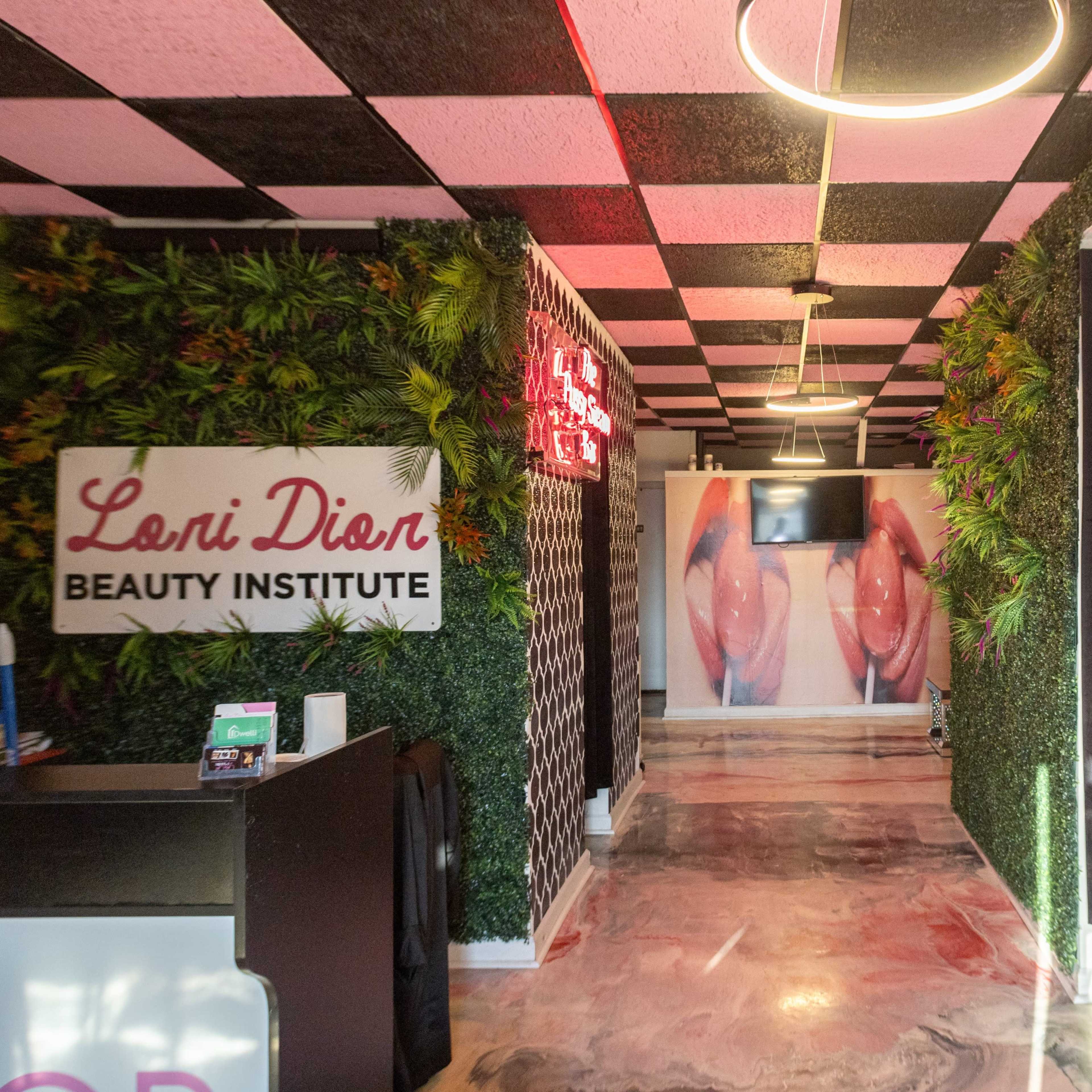 A hallway in the Loni Dion Beauty Institute featuring wall designs with pink and black colors and greenery along the sides.