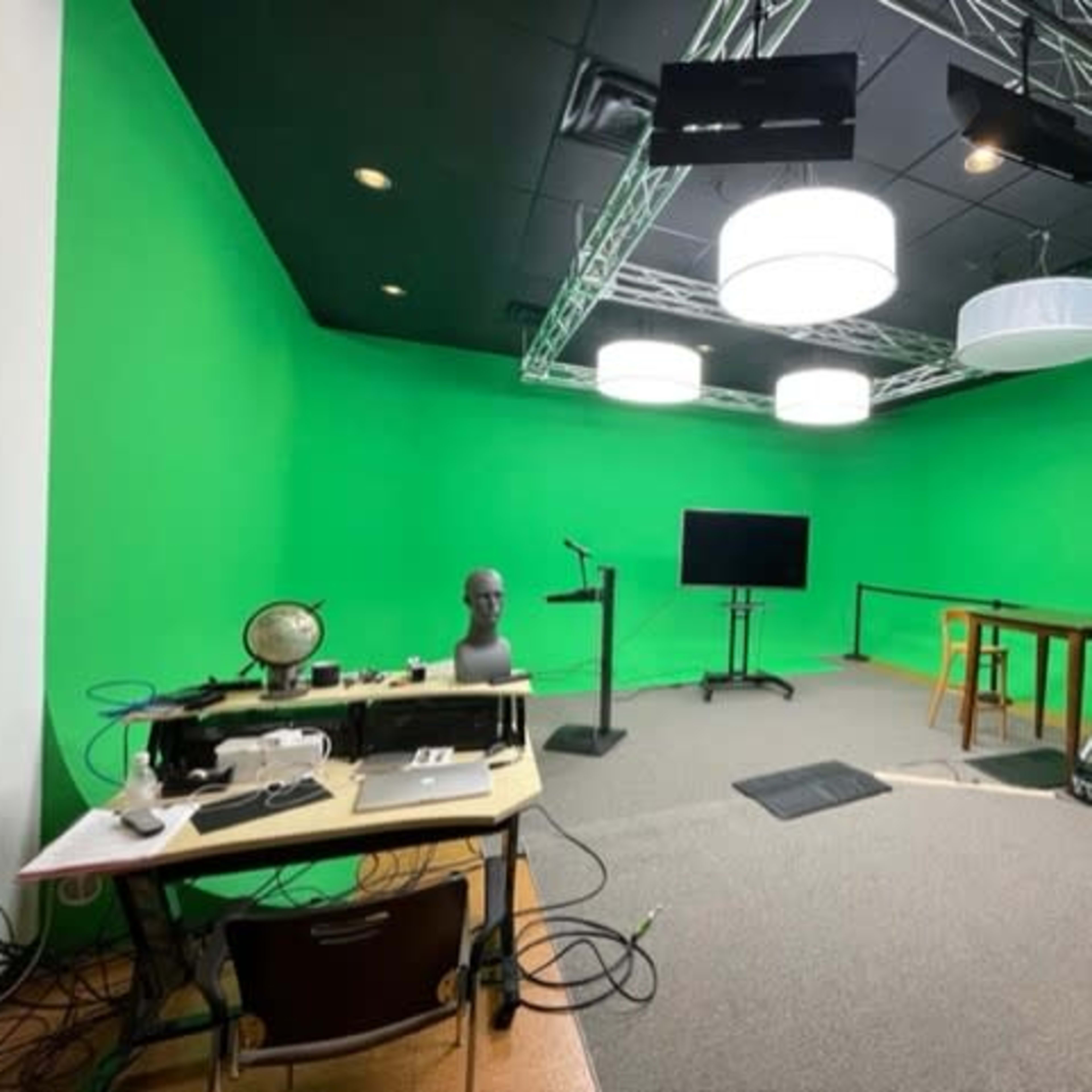 A green-screen studio with various lighting fixtures, a camera setup, and a desk with equipment.