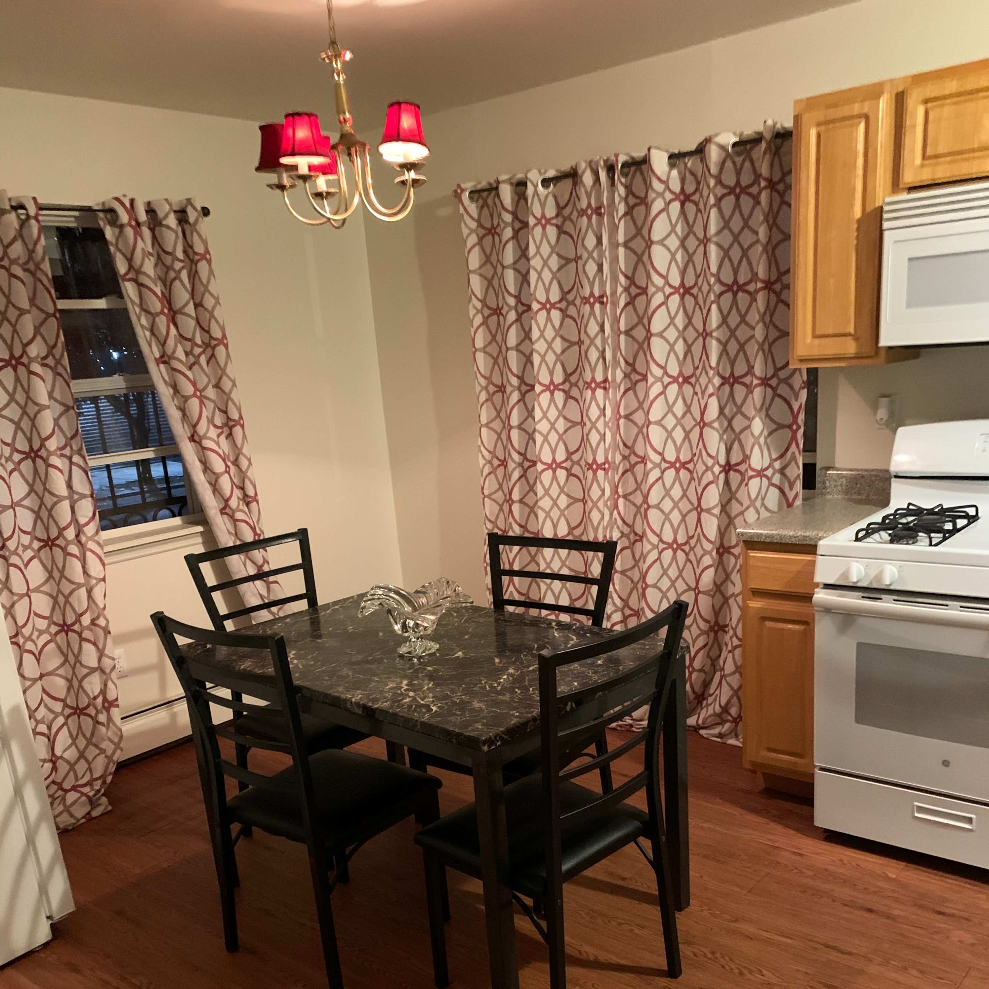A kitchen features a round black table with four chairs, a stove, and cabinets, all accompanied by red and white patterned curtains.
