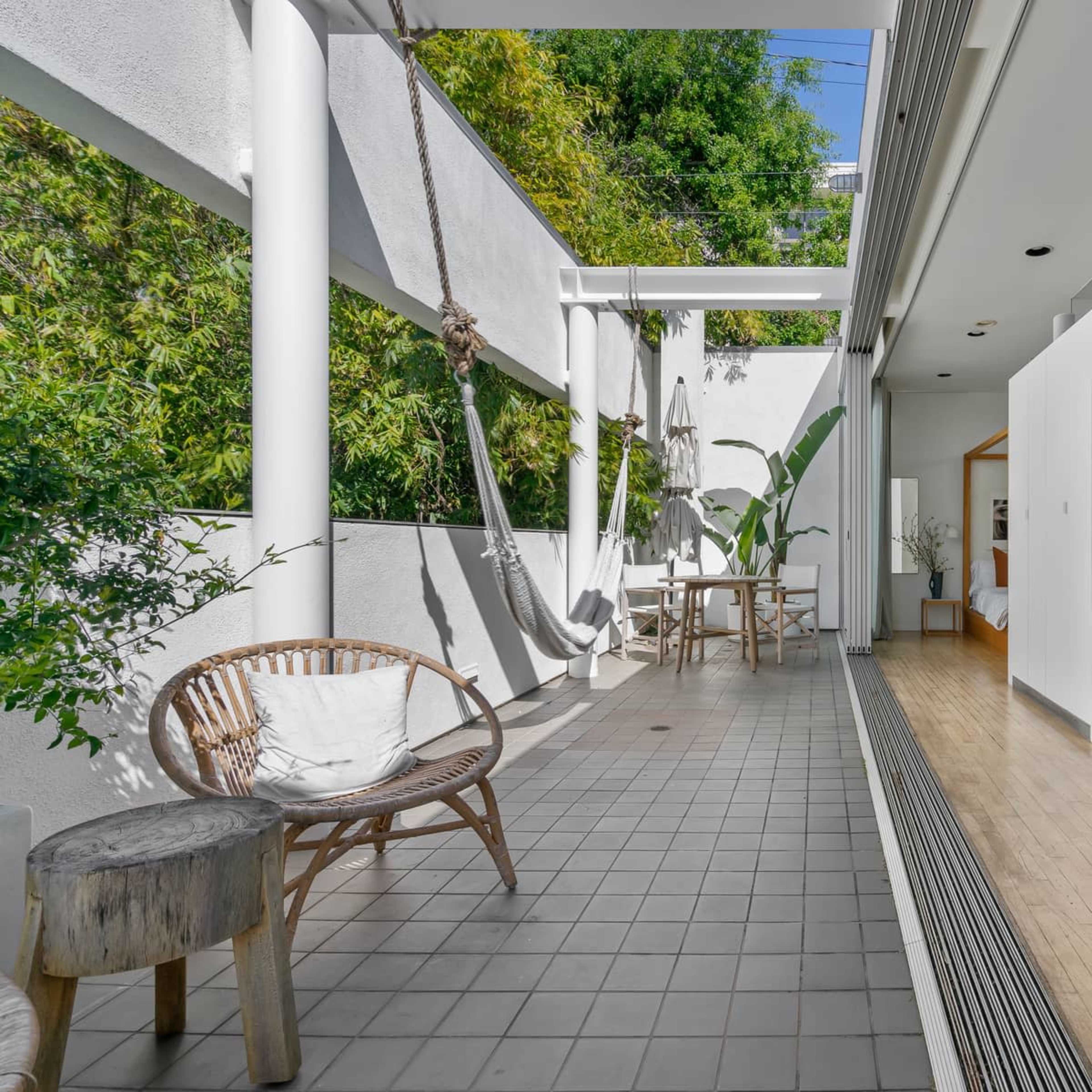 A modern outdoor and indoor living area featuring a tiled floor, hanging hammocks, and a view of greenery.