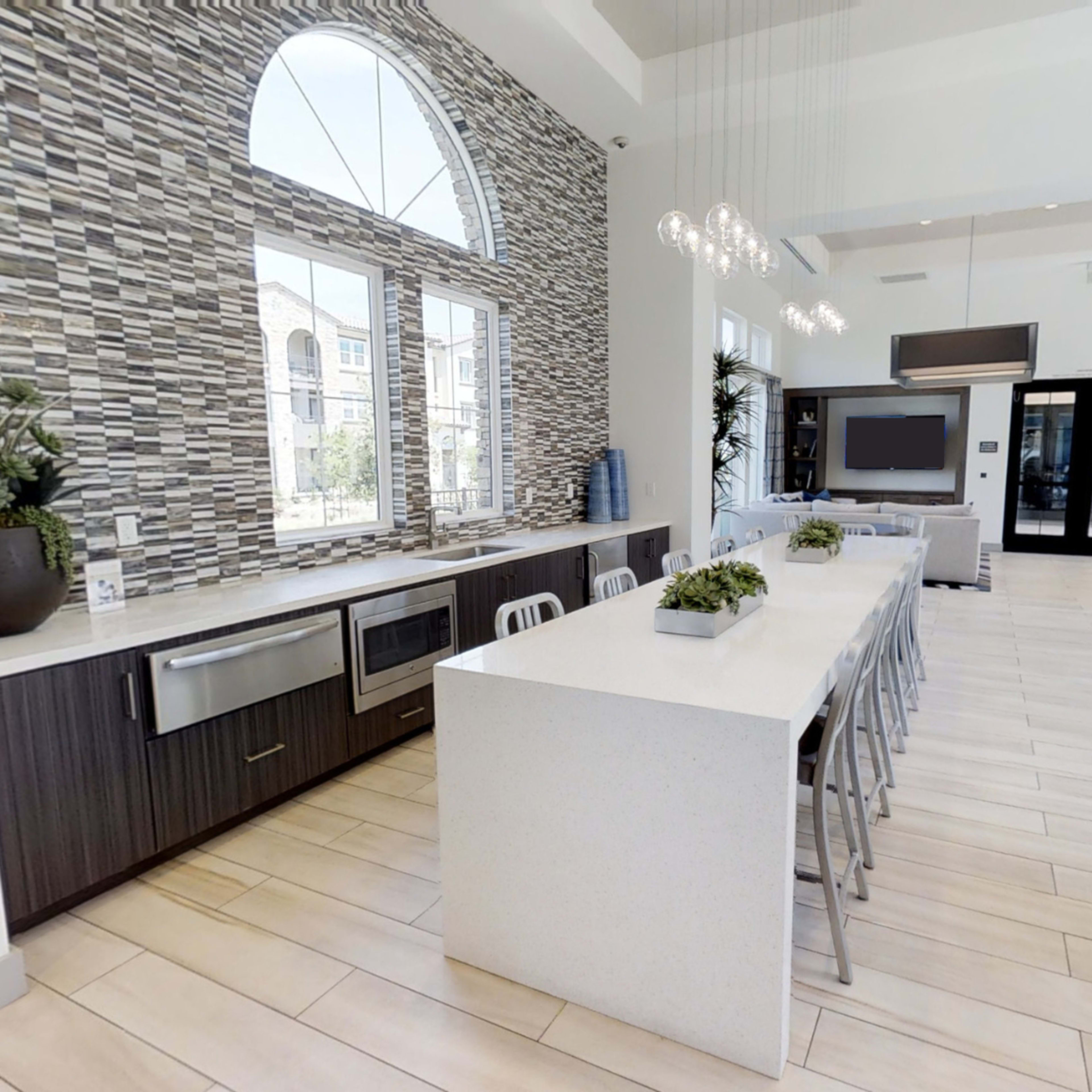 A modern kitchen features a long central island with seating, sleek cabinetry, and large windows that provide natural light.