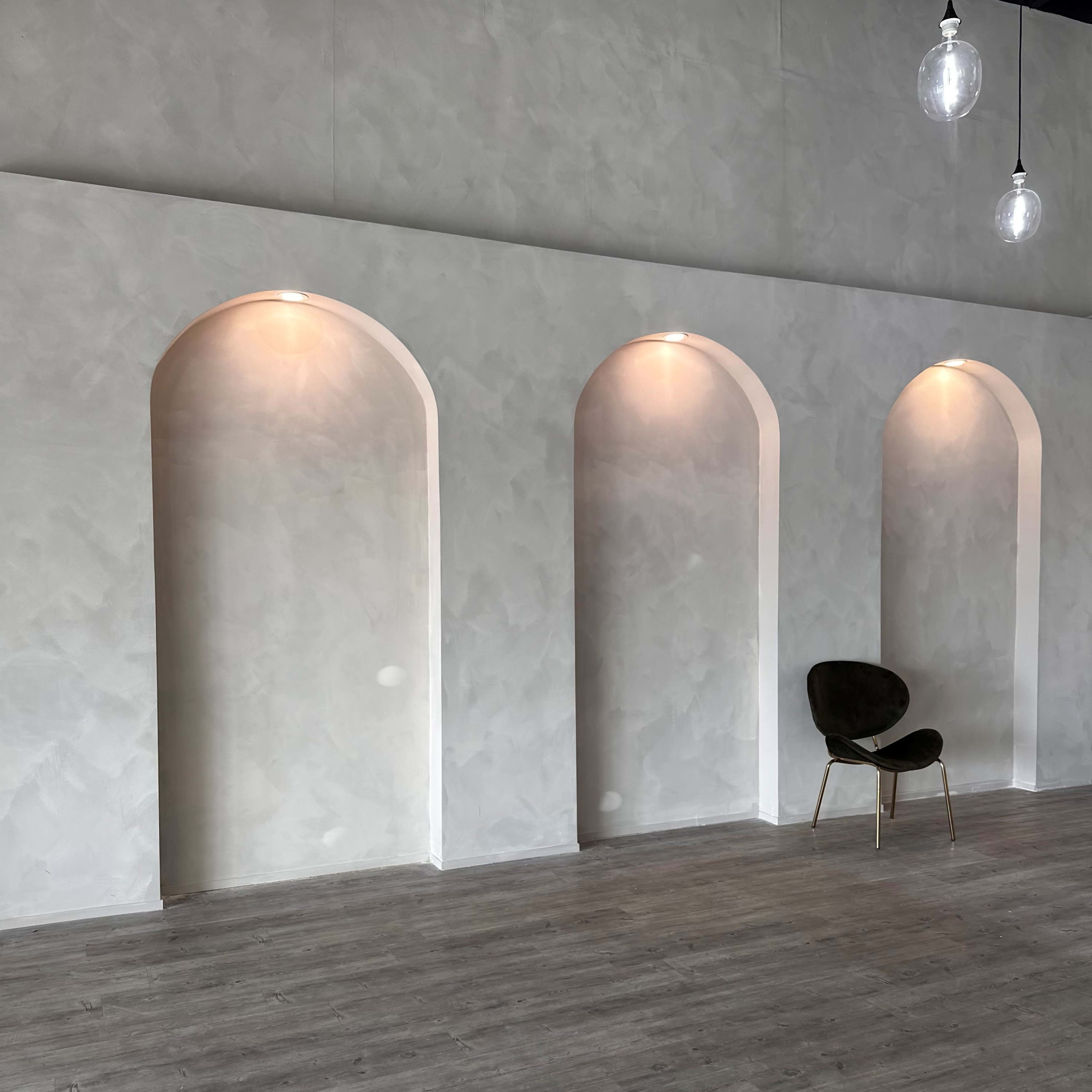 A minimalist interior space featuring three arched wall recesses and a single chair placed against a light-colored textured wall.