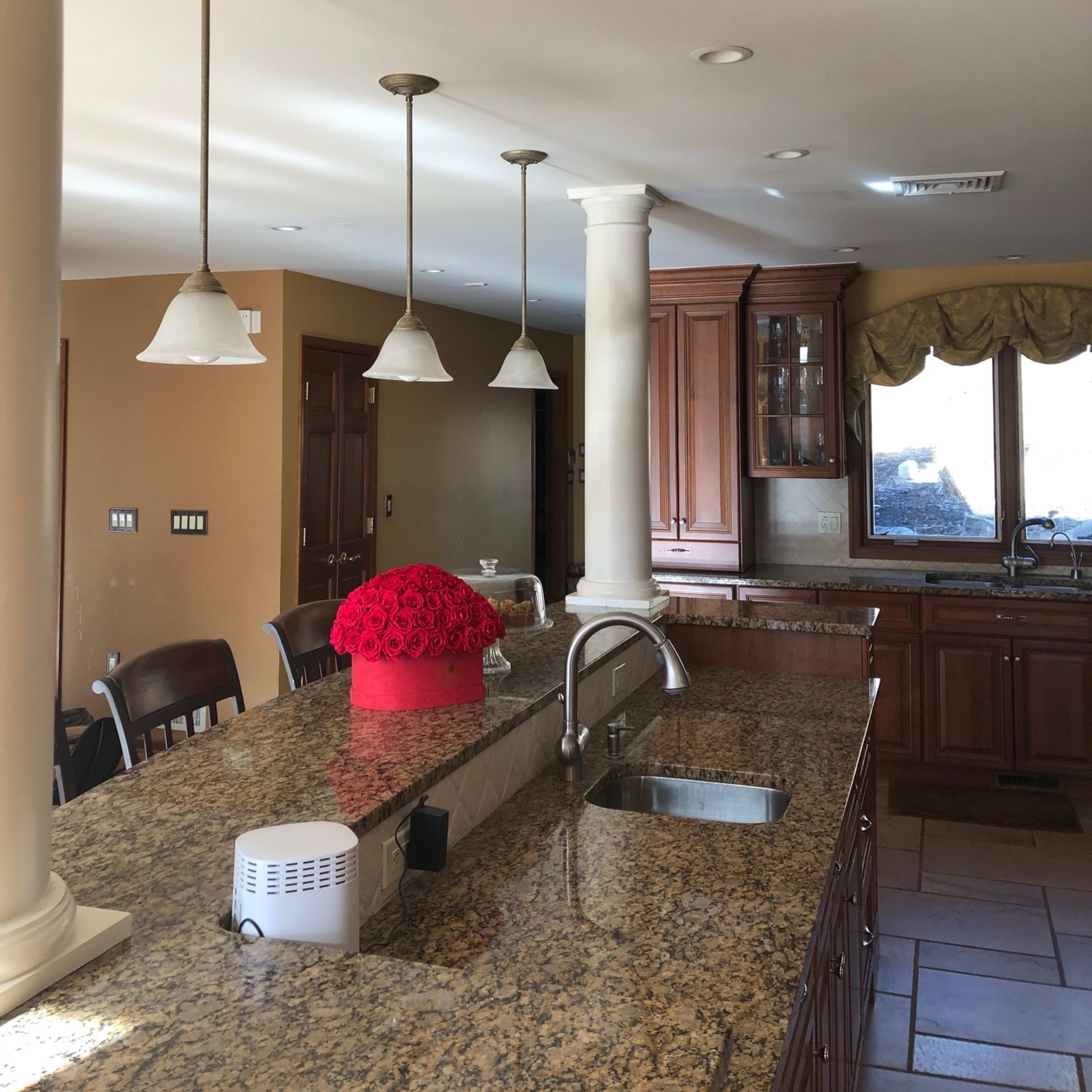 A kitchen with granite countertops, pendant lighting, and wooden cabinetry, featuring a vase of red flowers on the island.