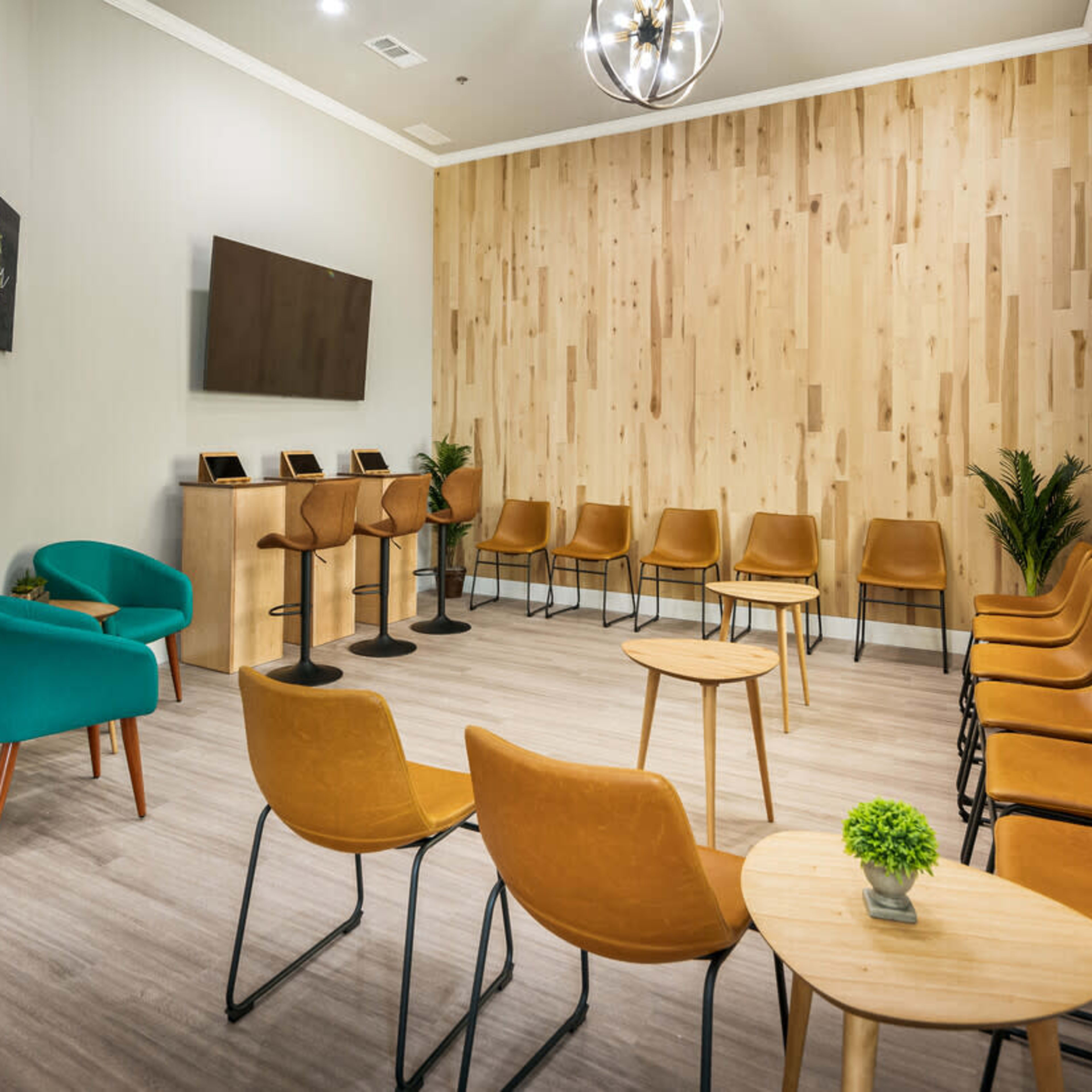 A welcoming waiting room features a mix of brown and teal seating arranged around small wooden tables against a wooden accent wall.