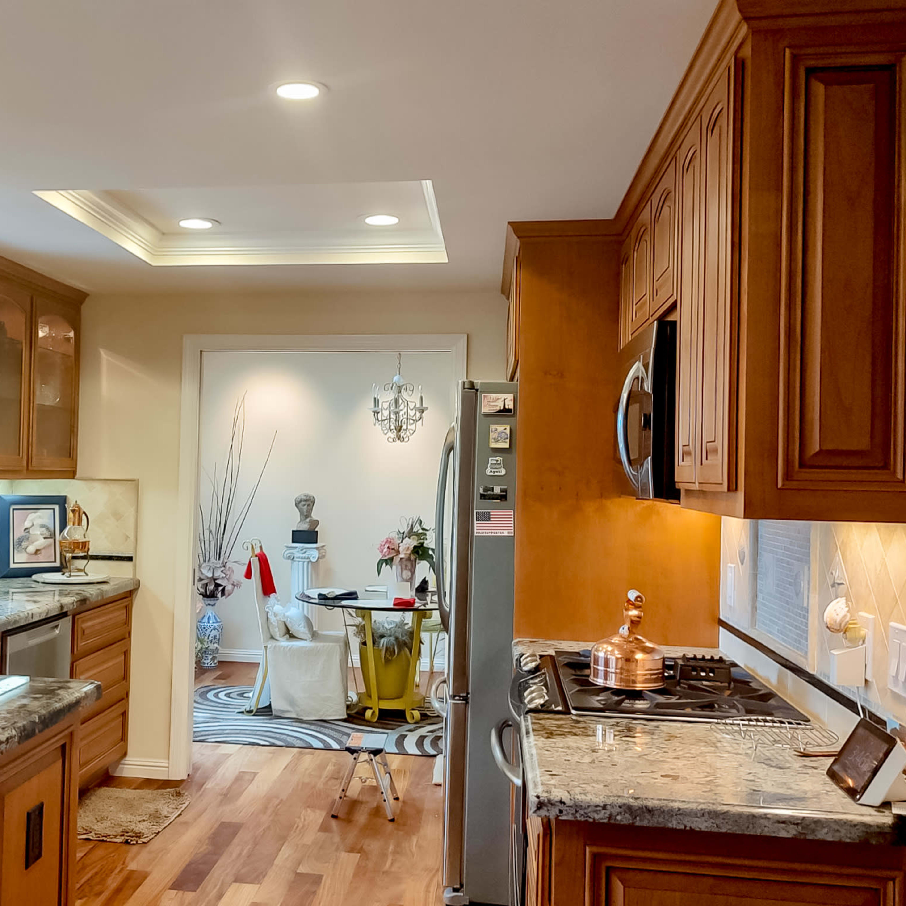 A modern kitchen features wooden cabinets, granite countertops, and stainless-steel appliances, with an adjoining dining area visible in the background.