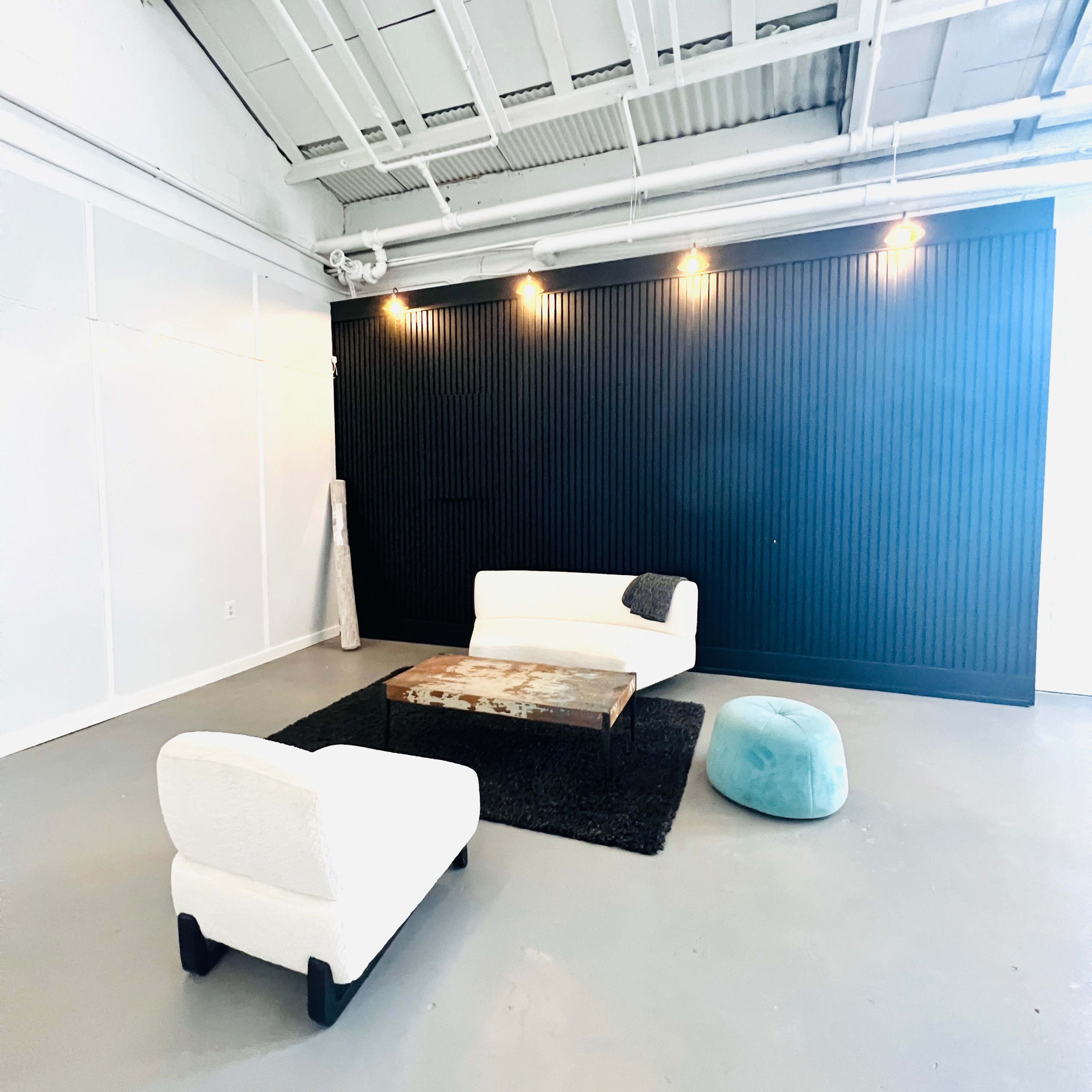 A modern living room with a white sofa and armchair around a wooden coffee table, set against a contrasting black wall with overhead lighting.